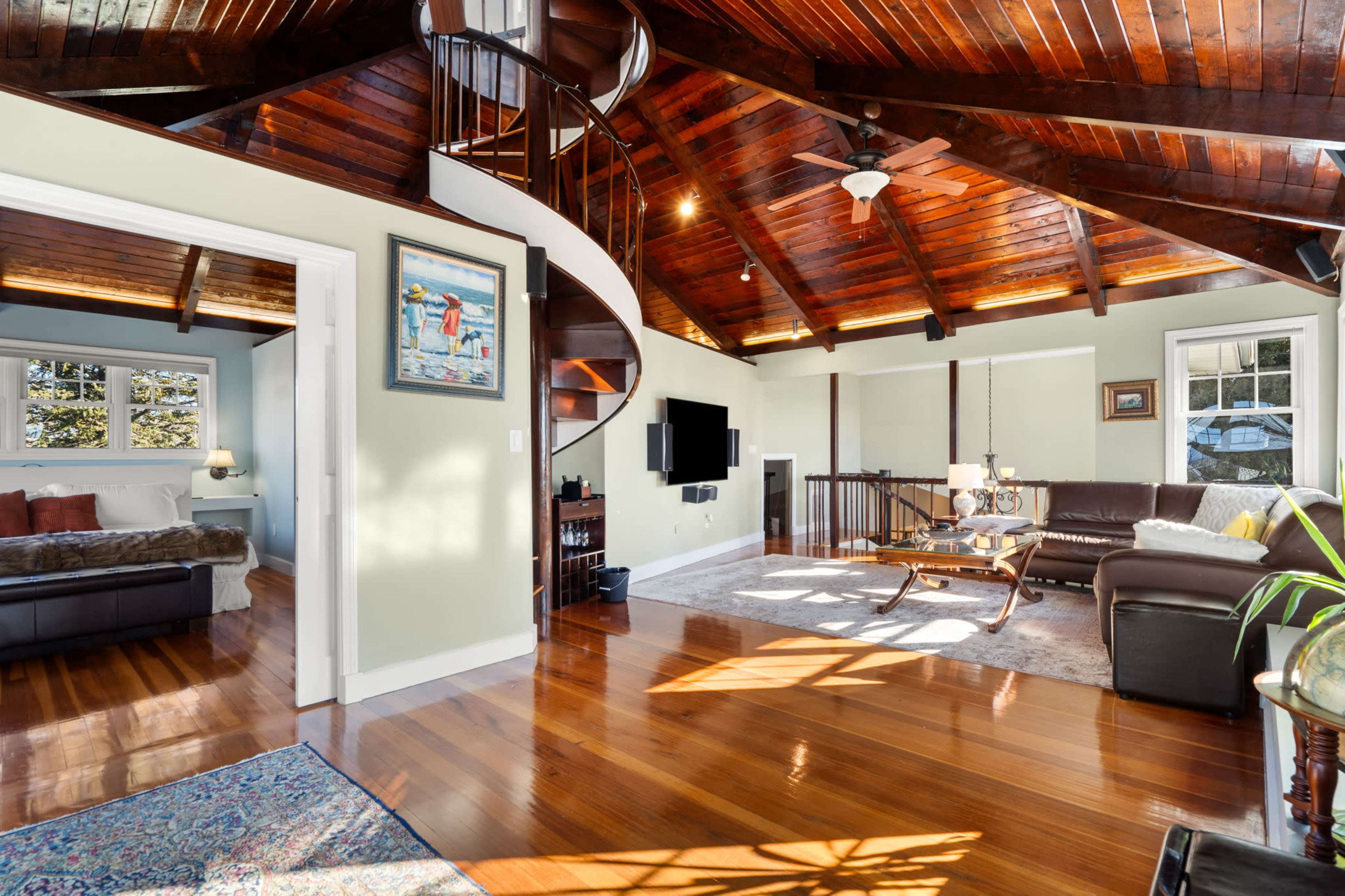 A spacious living room with a spiral staircase, hardwood floors, and large windows that allow plenty of natural light.