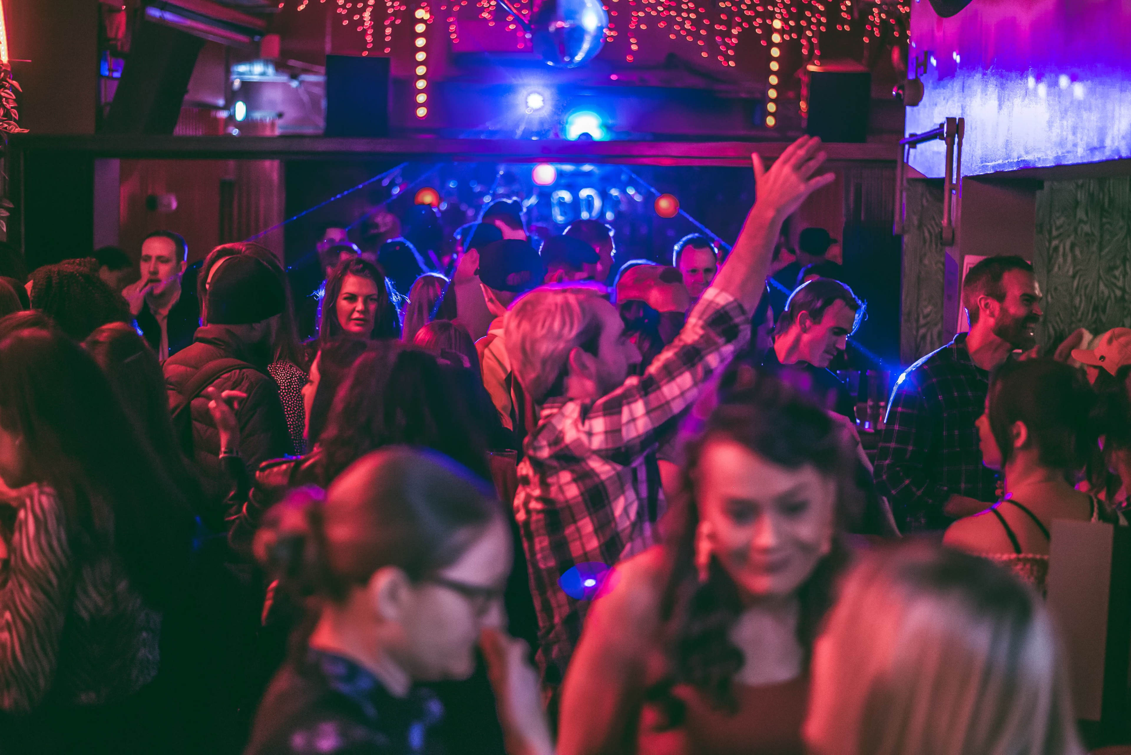 A crowded dance floor filled with people enjoying a lively party under colorful lights.