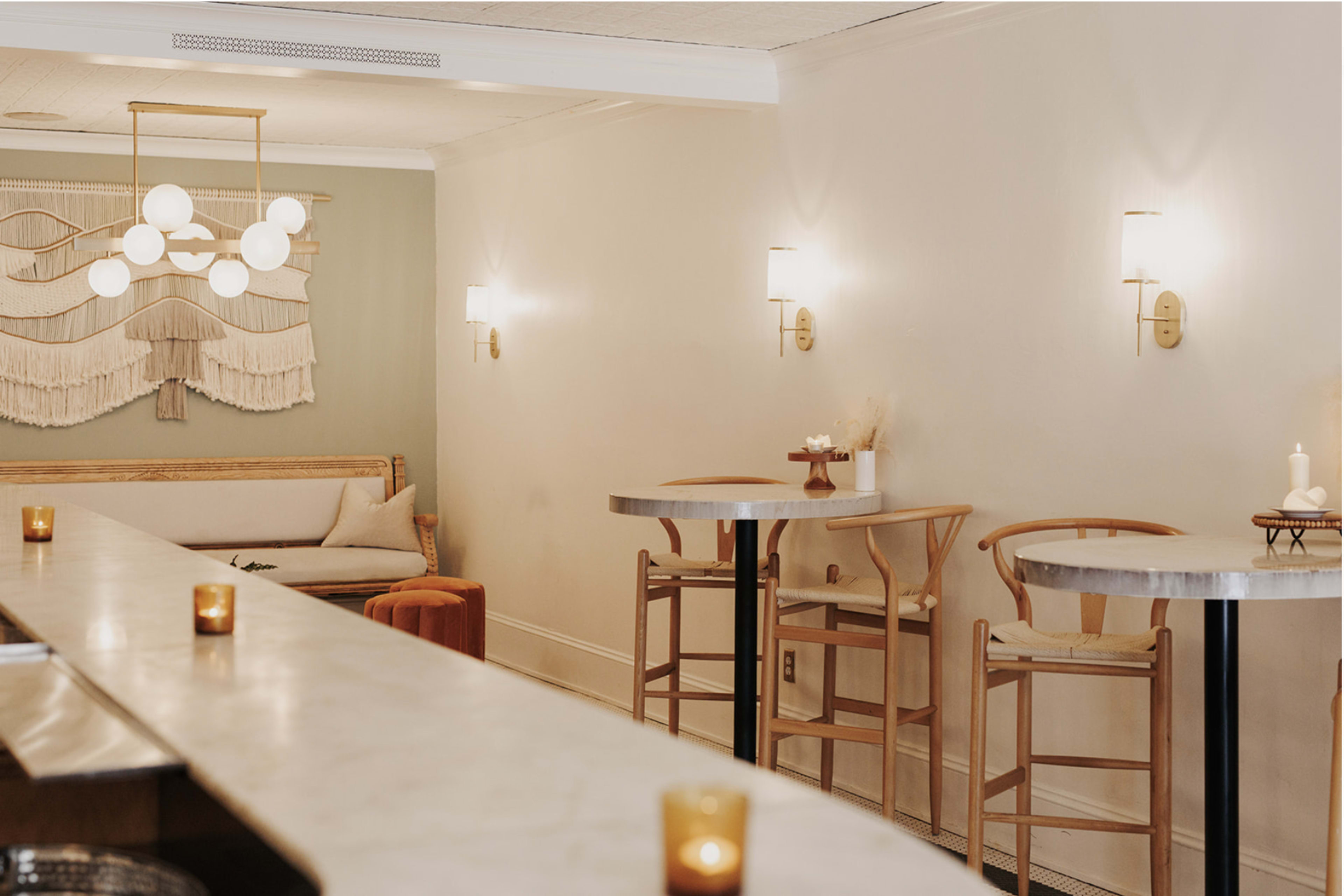 A modern, minimalist interior of a café featuring light-colored walls, a bar with a marble countertop, and a few wooden seating areas illuminated by soft wall sconces.