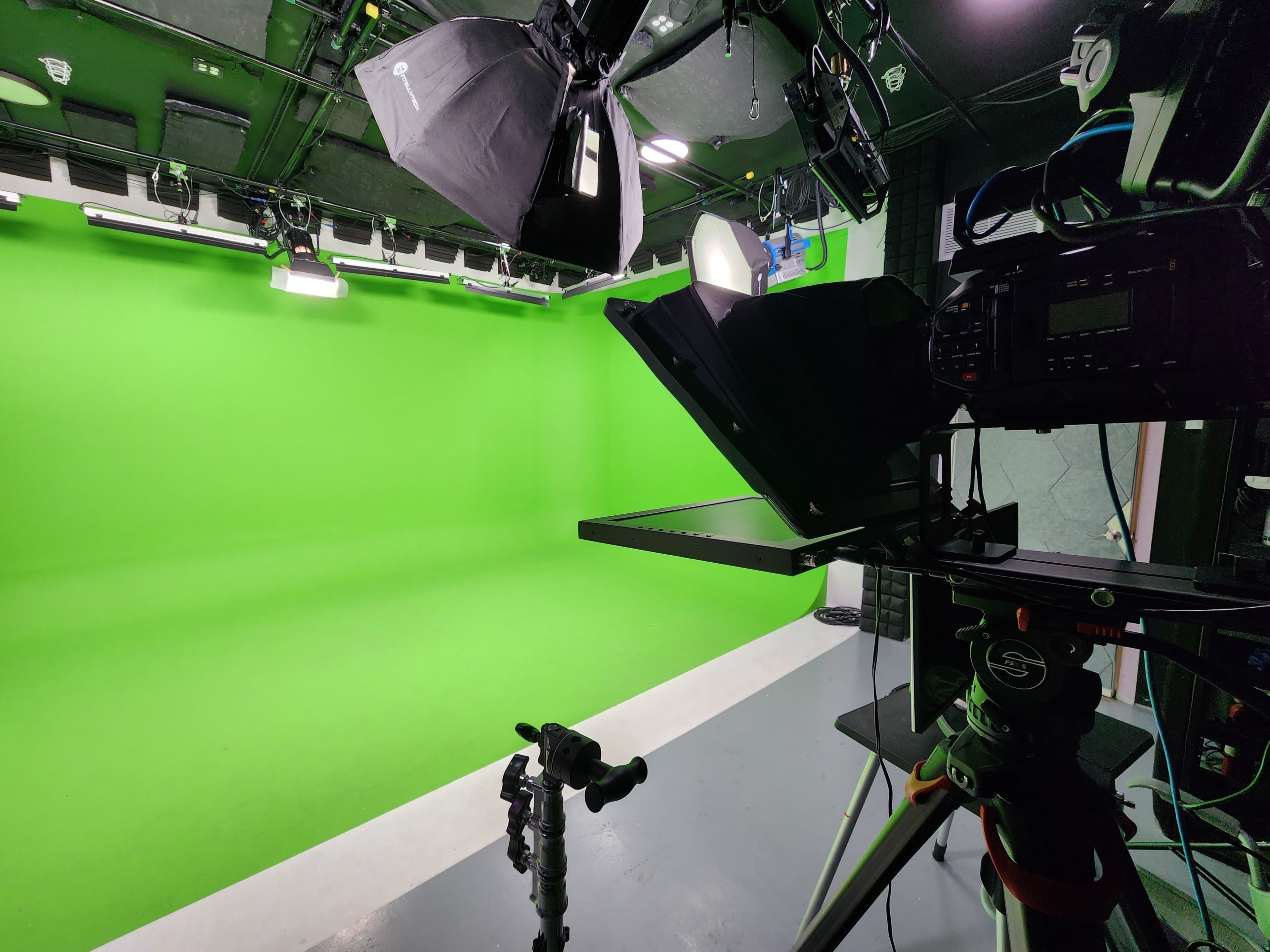 A green screen studio with lighting equipment and a camera setup on a tripod.