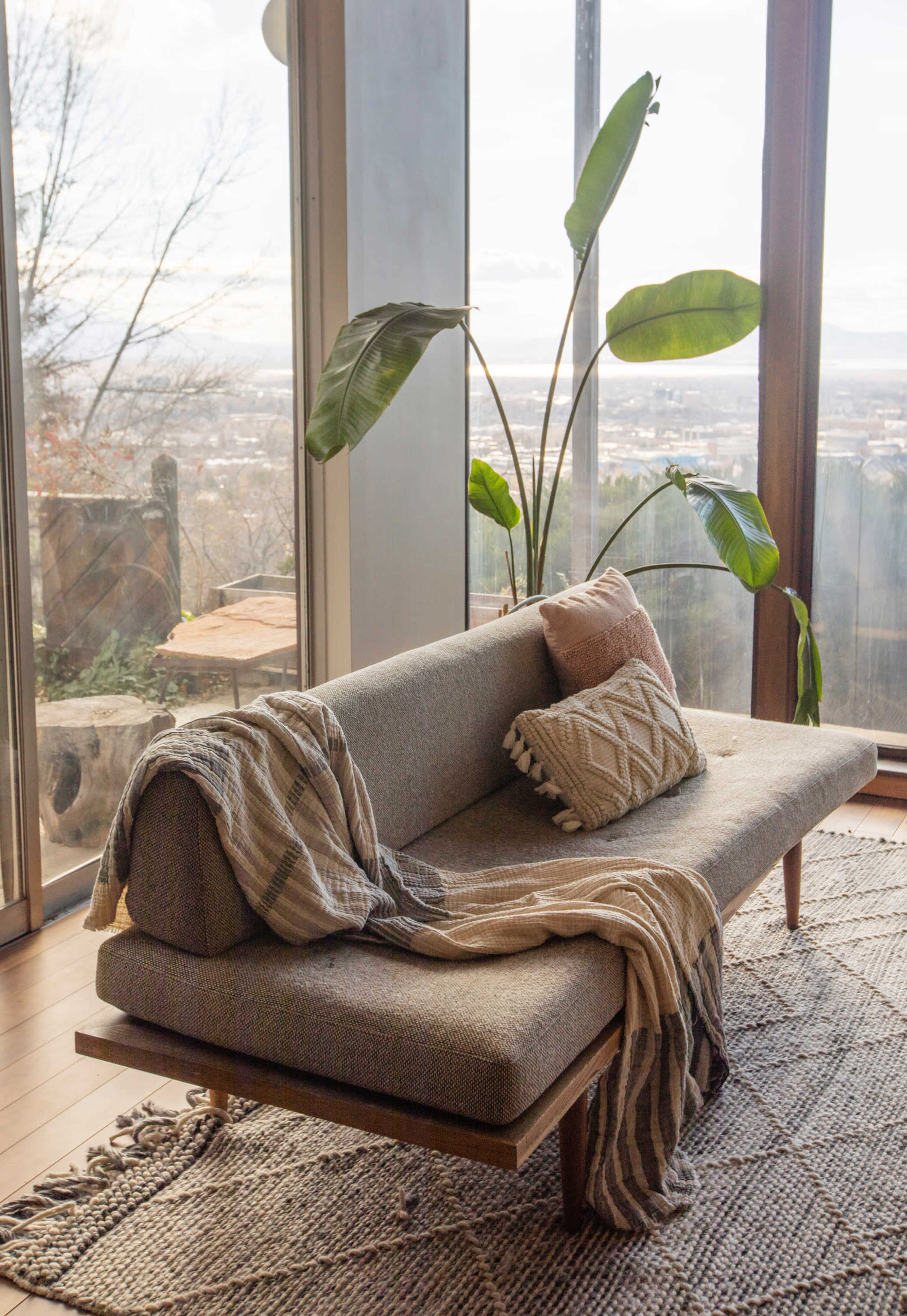 A modern sofa with a textured throw and cushions is positioned near large windows overlooking a scenic view.