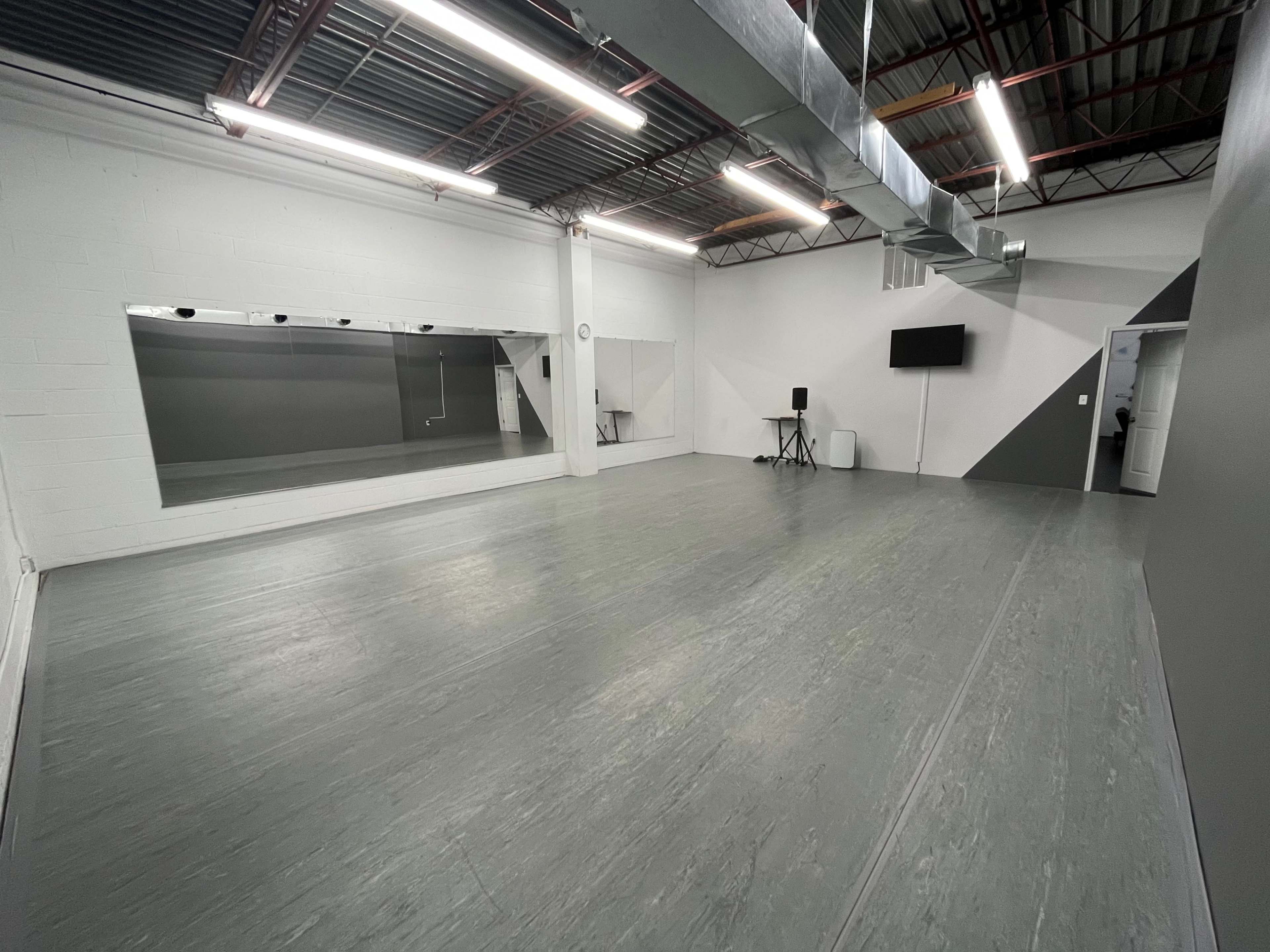 A spacious, empty studio with gray walls, a large mirror, and minimal furnishings.