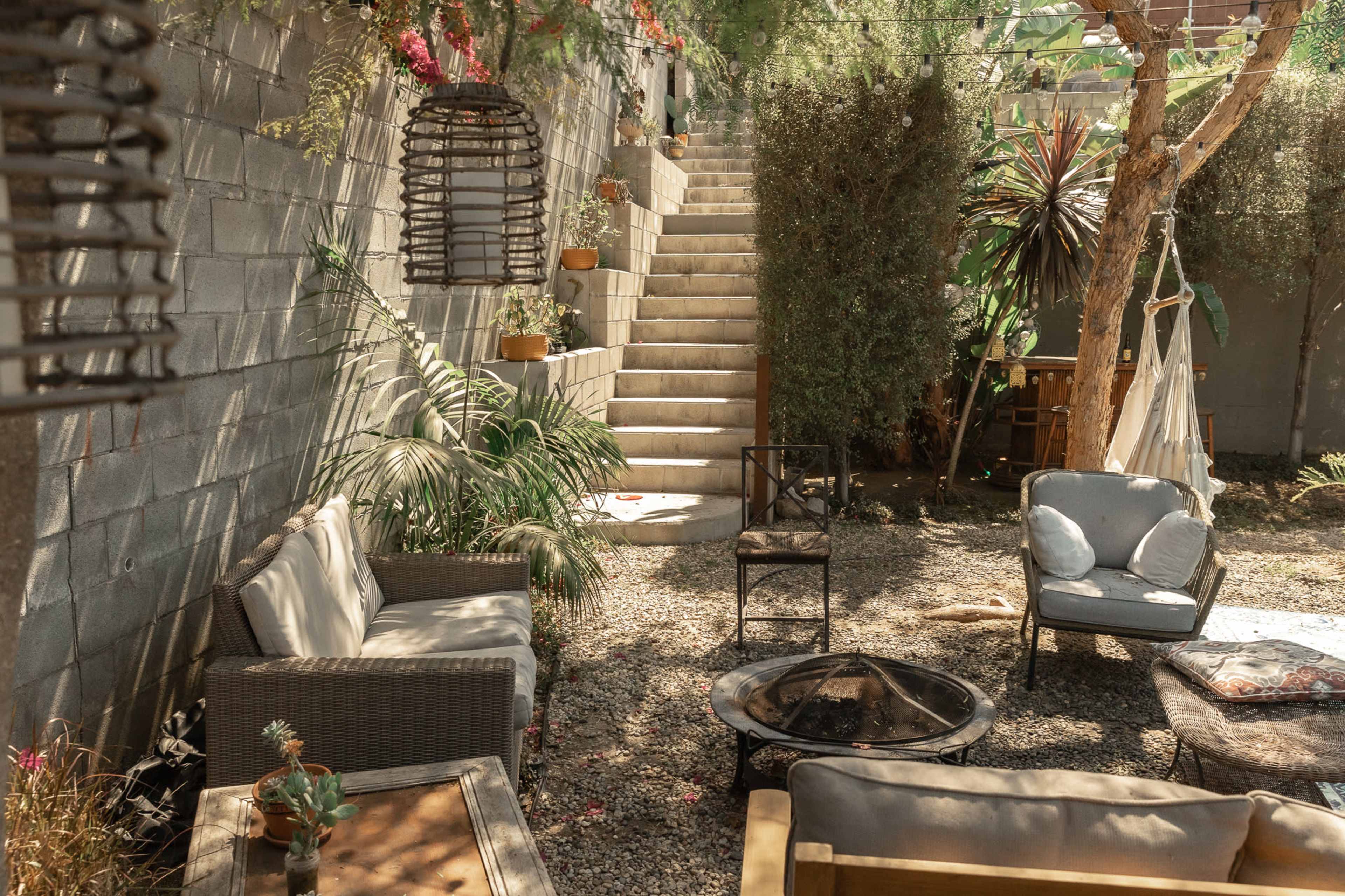A cozy garden area with seating arrangements, a fire pit, and stairs leading to an elevated section surrounded by greenery.