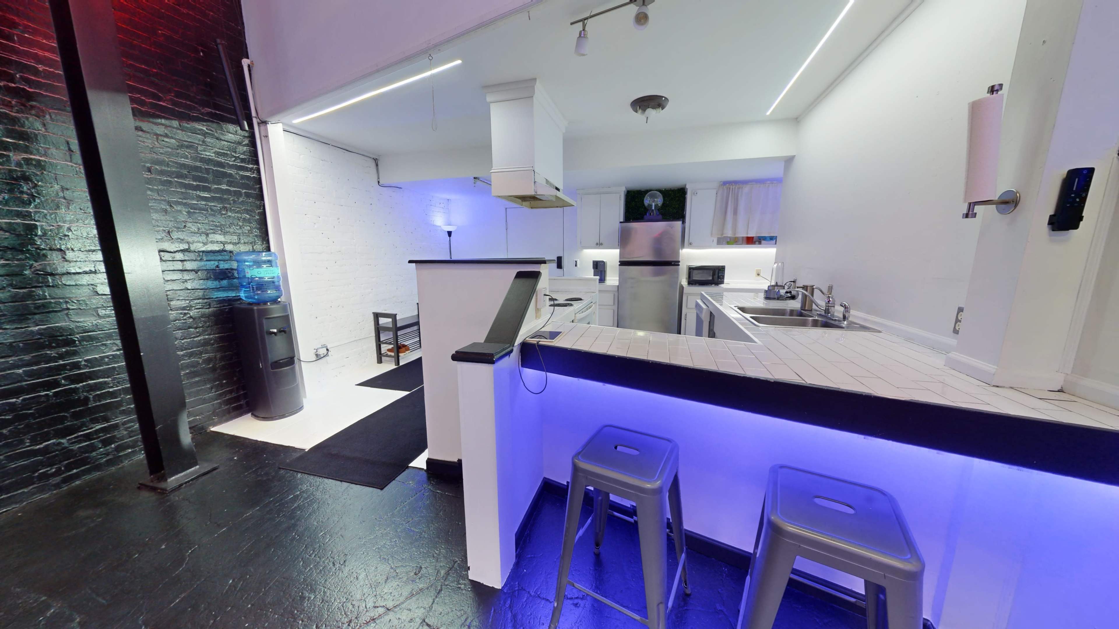 A modern kitchen area with stainless steel appliances, a bar-style counter with metal stools, and contrasting black and white walls.