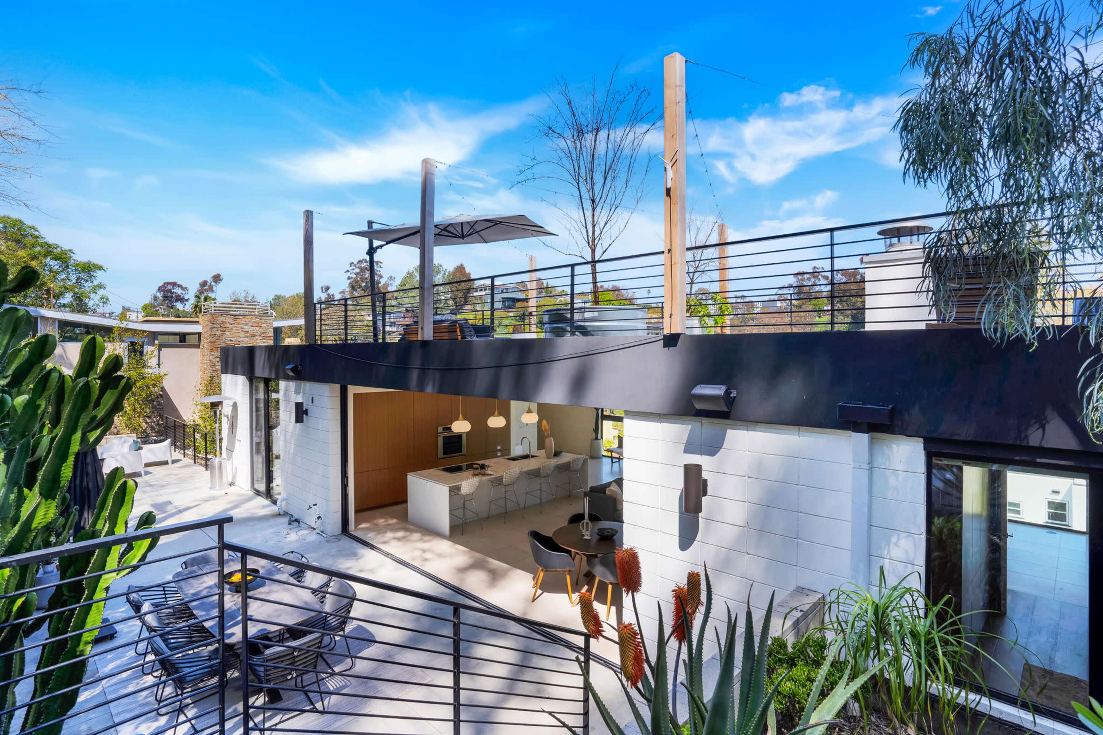 A modern building with a rooftop terrace features a spacious outdoor dining area and a sleek kitchen visible through large windows.