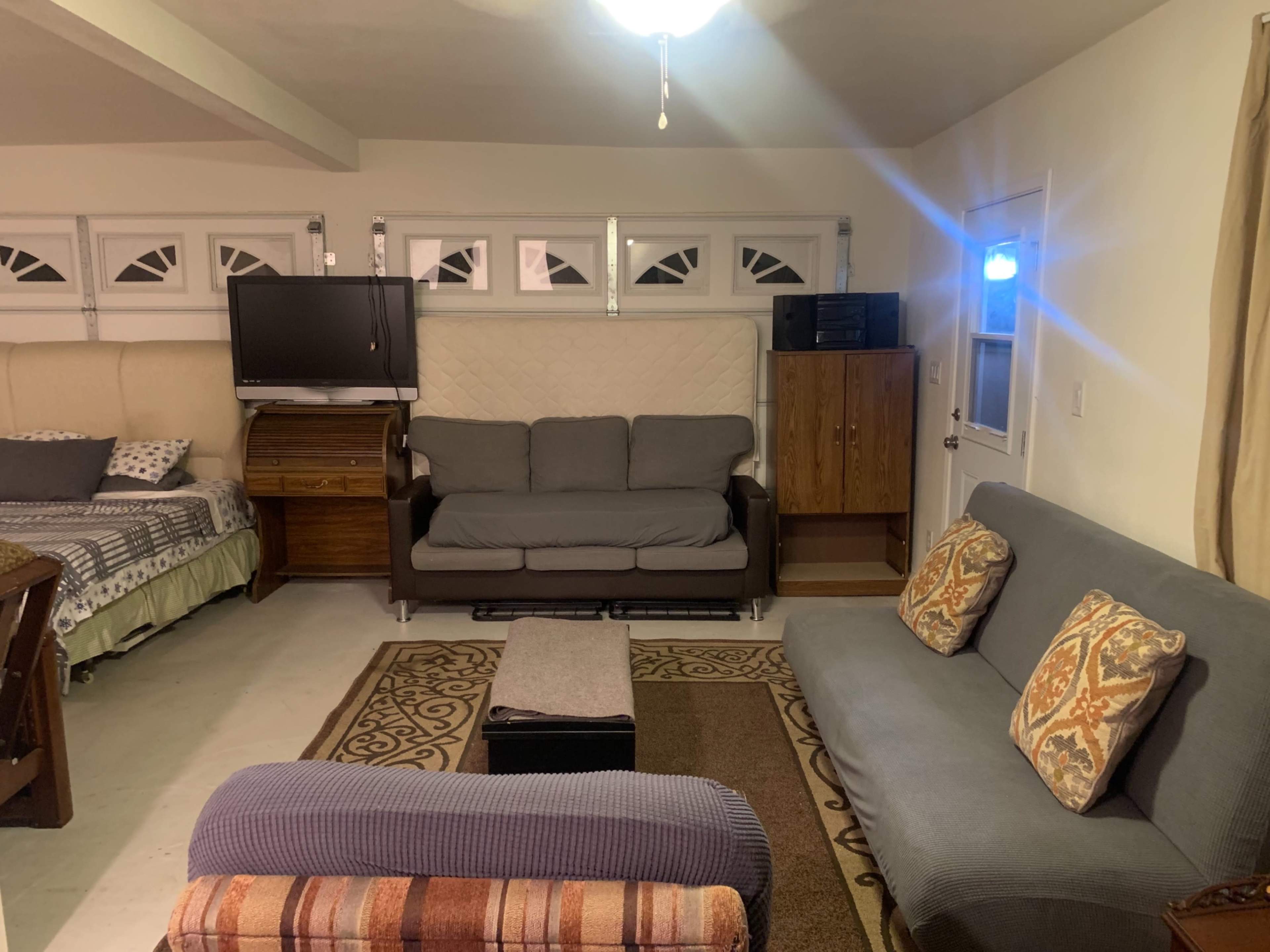 A living room with two sofas, a coffee table, a television, and a doorway leading to another room, all arranged against a backdrop of light-colored walls and a ceiling fan.