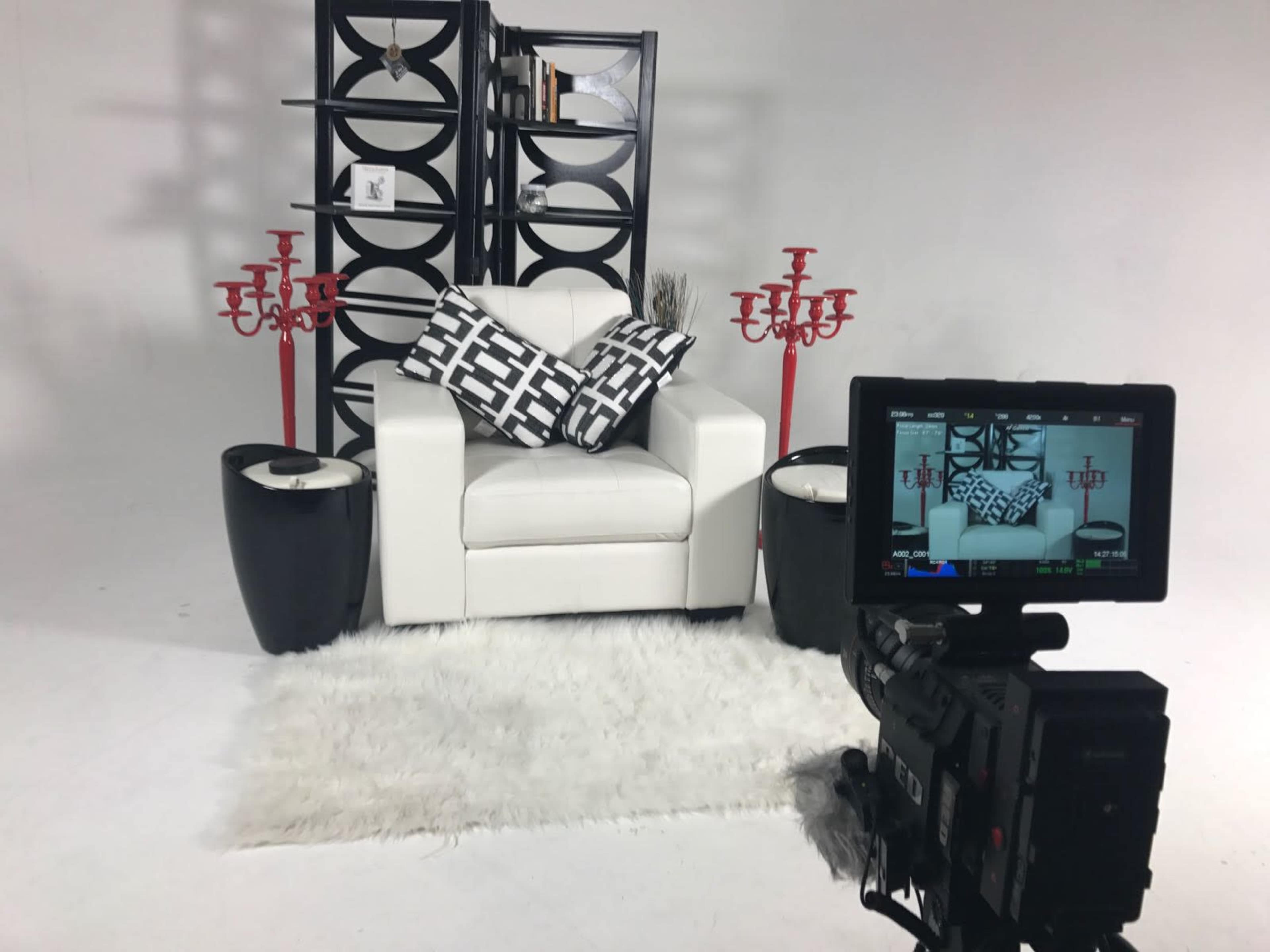 A modern white armchair with patterned black and white pillows, flanked by two black side tables and red candelabras, against a minimalist backdrop.