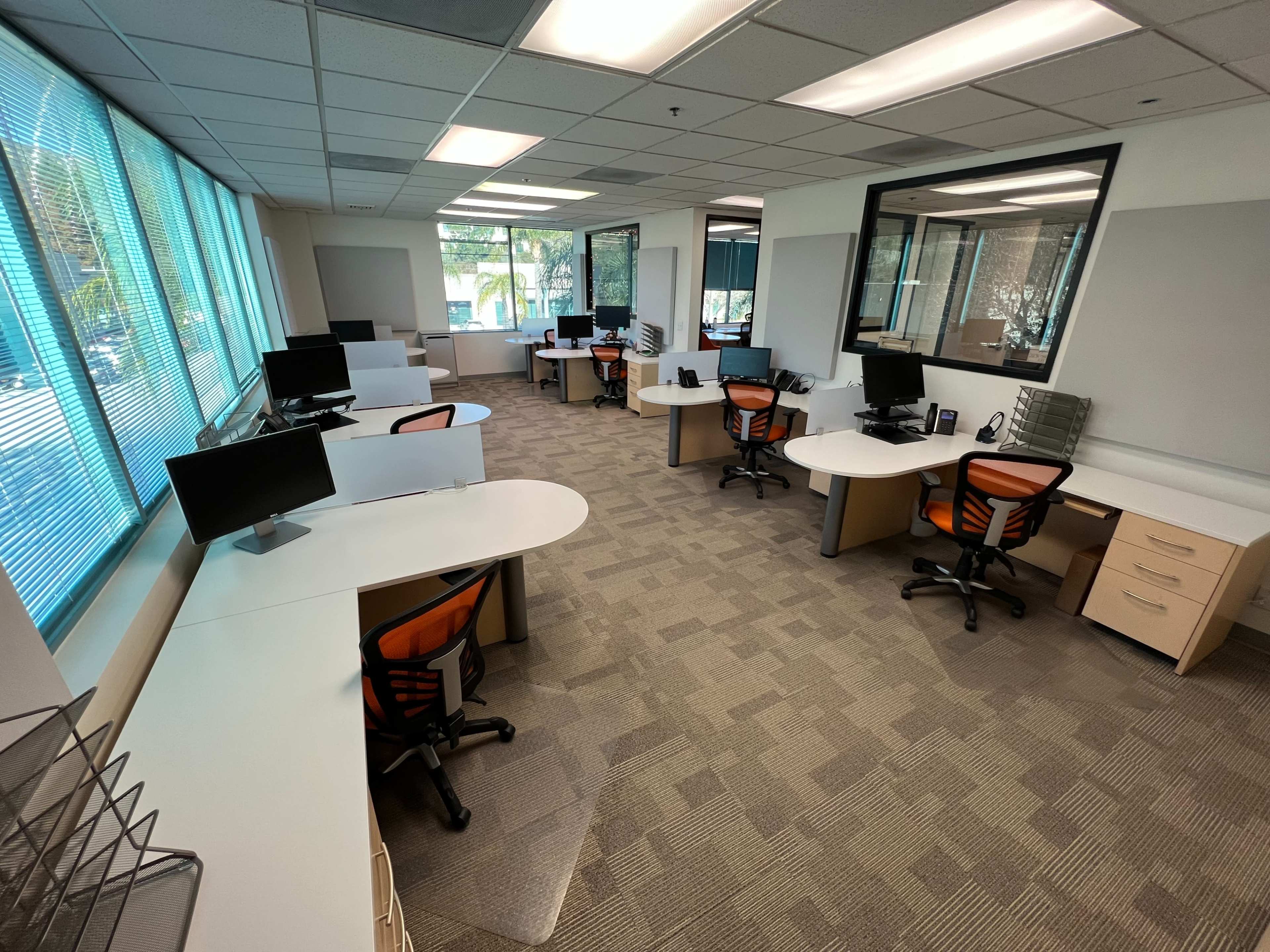 A spacious, modern office with several desks equipped with computers and ergonomic chairs, illuminated by large windows.