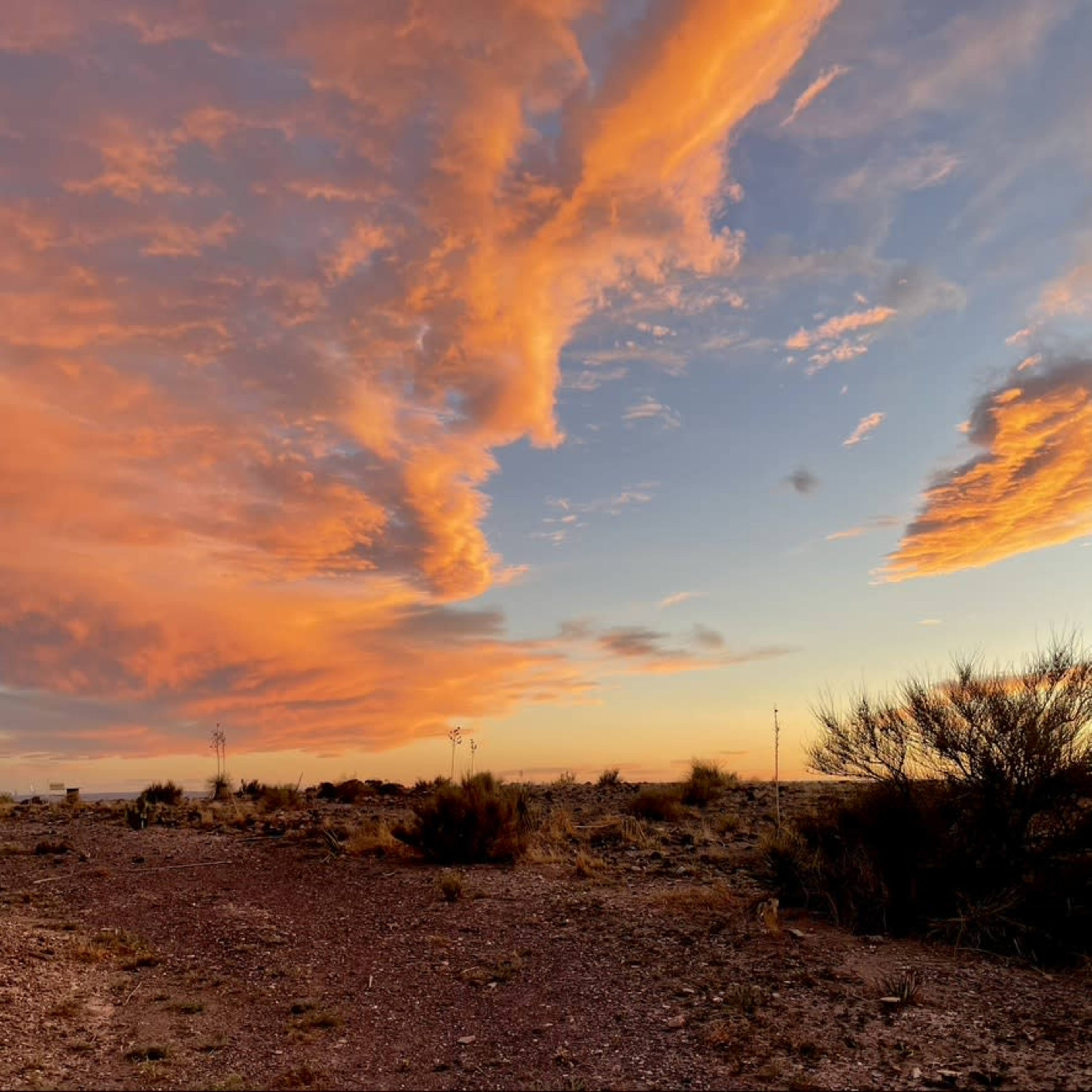 The scene shows a colorful sky at sunset with scattered clouds above an arid landscape.