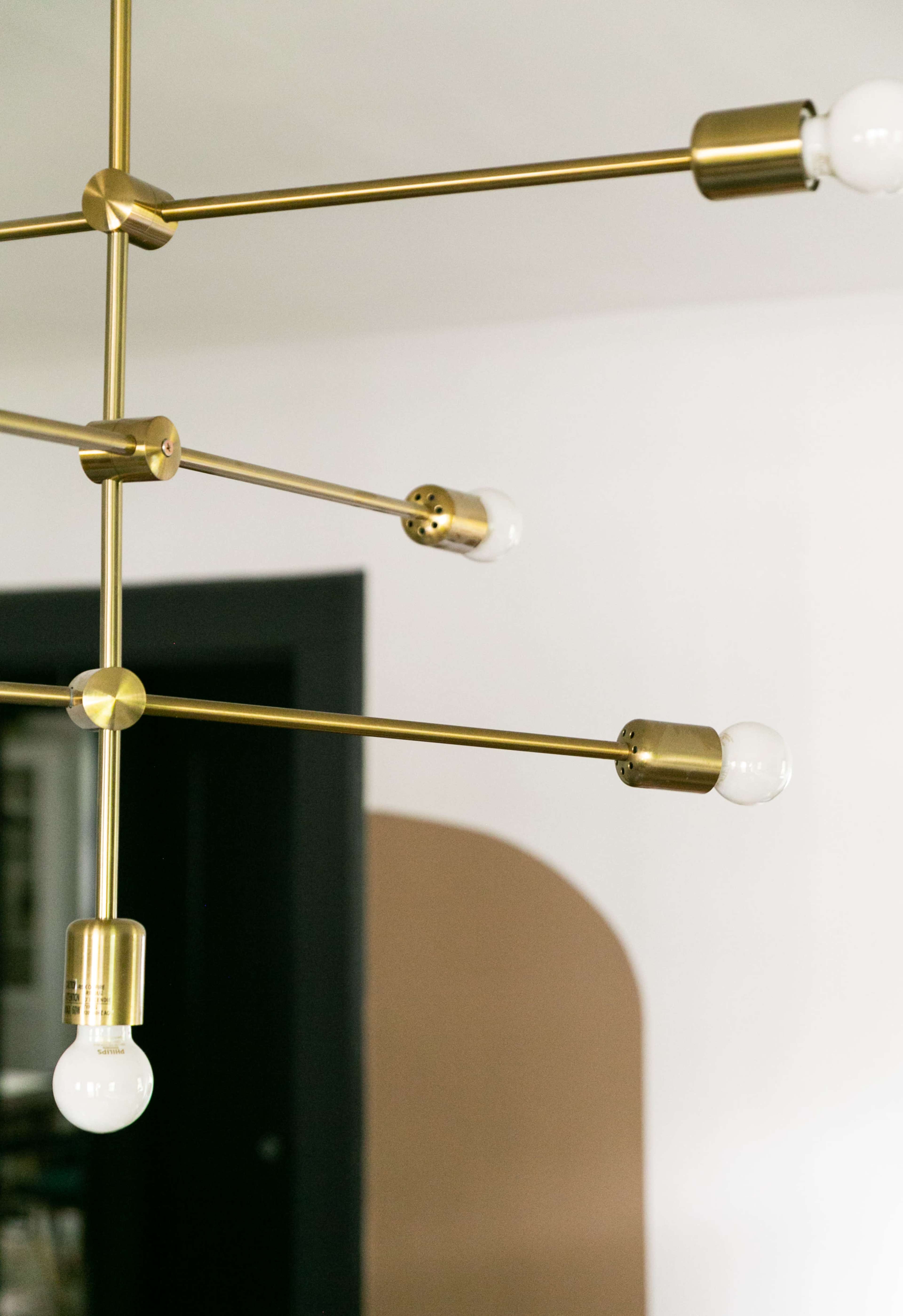 A modern brass chandelier with multiple light bulbs arranged in an intersecting pattern.