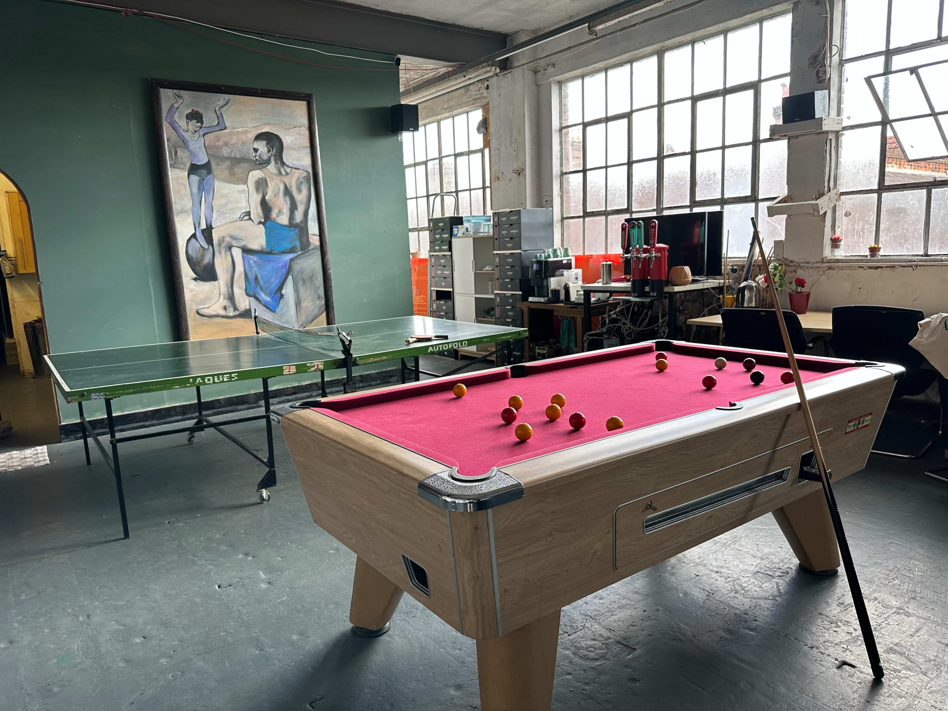 A recreational room featuring a pink-felt pool table, a ping pong table, and a large painting on the wall.
