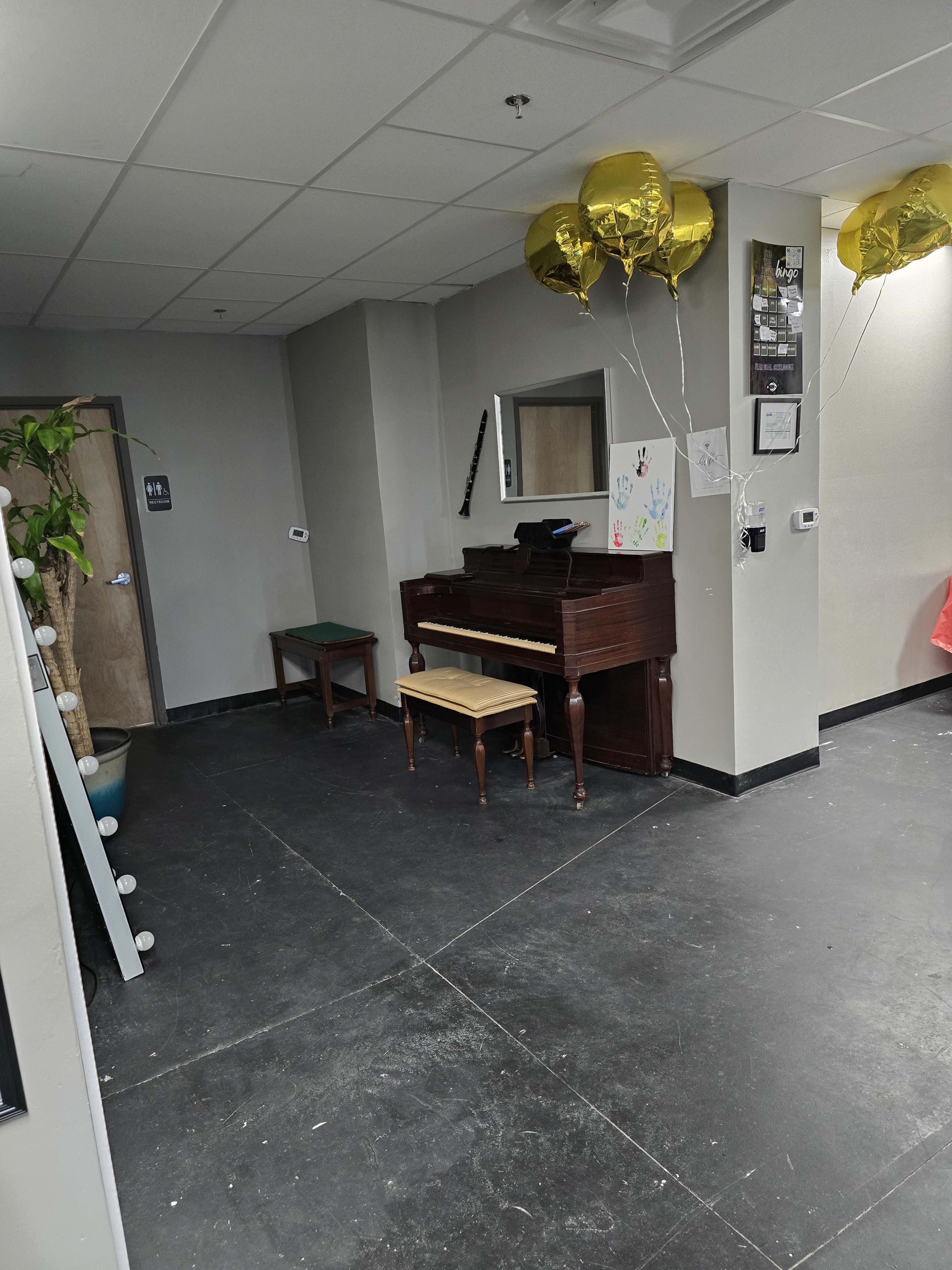 A small corner of a room featuring a wooden piano with a matching bench, a green chair, and three gold balloons on the right side.