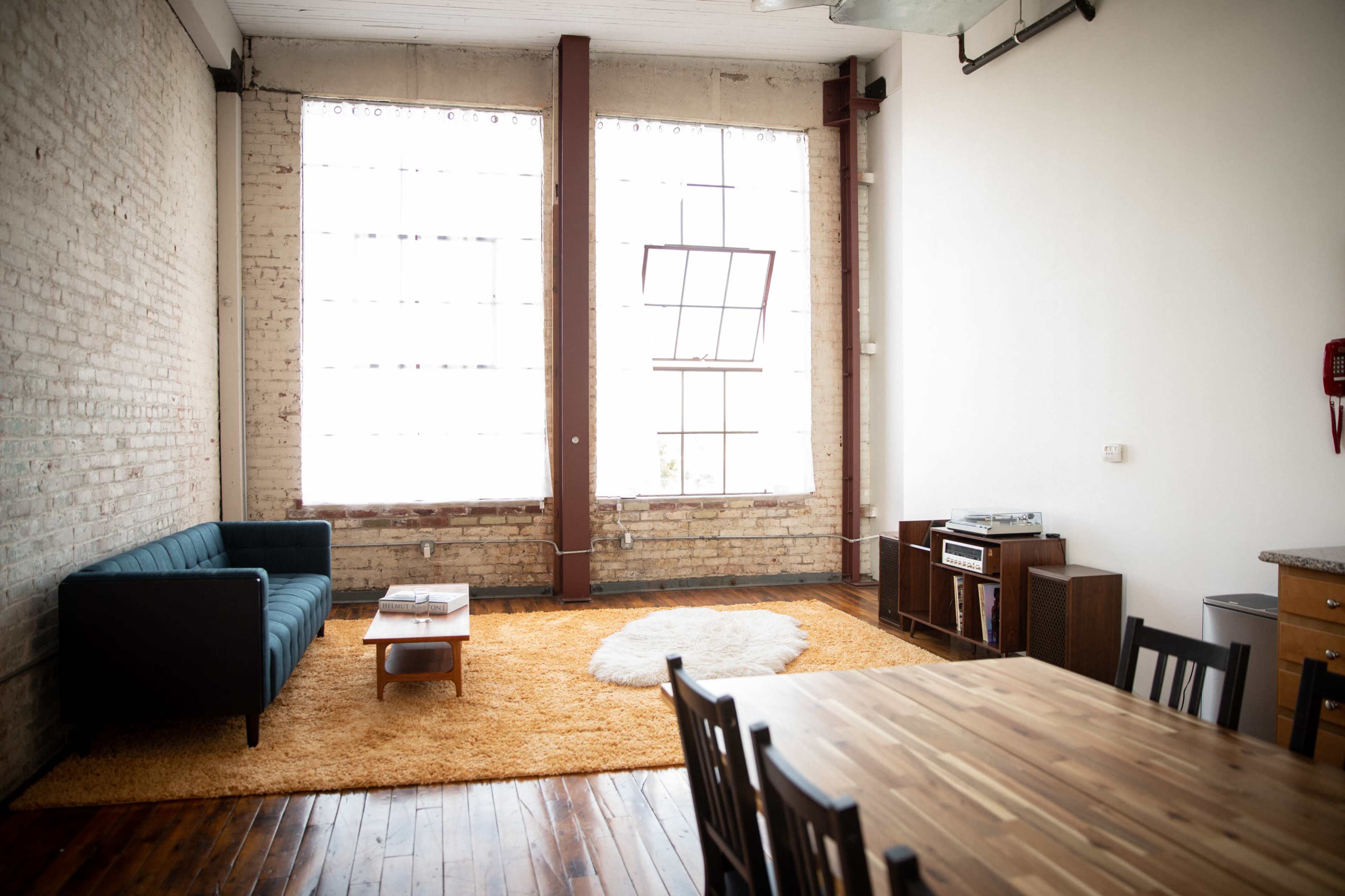A spacious room with large windows, a blue couch, a wooden dining table, and an orange rug on a wooden floor.