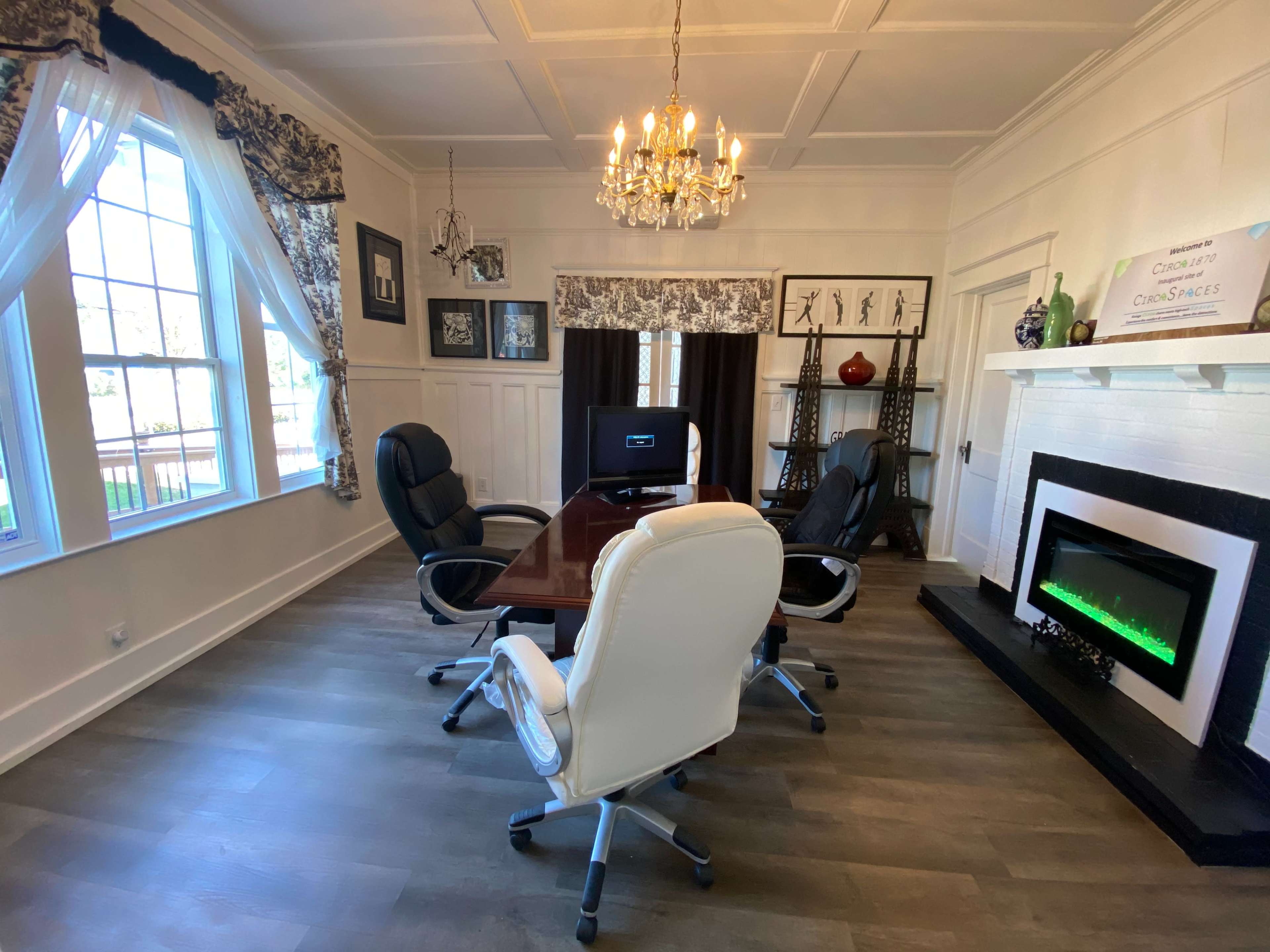 A well-lit office with a wooden conference table surrounded by four ergonomic chairs and a decorative electric fireplace against the wall.