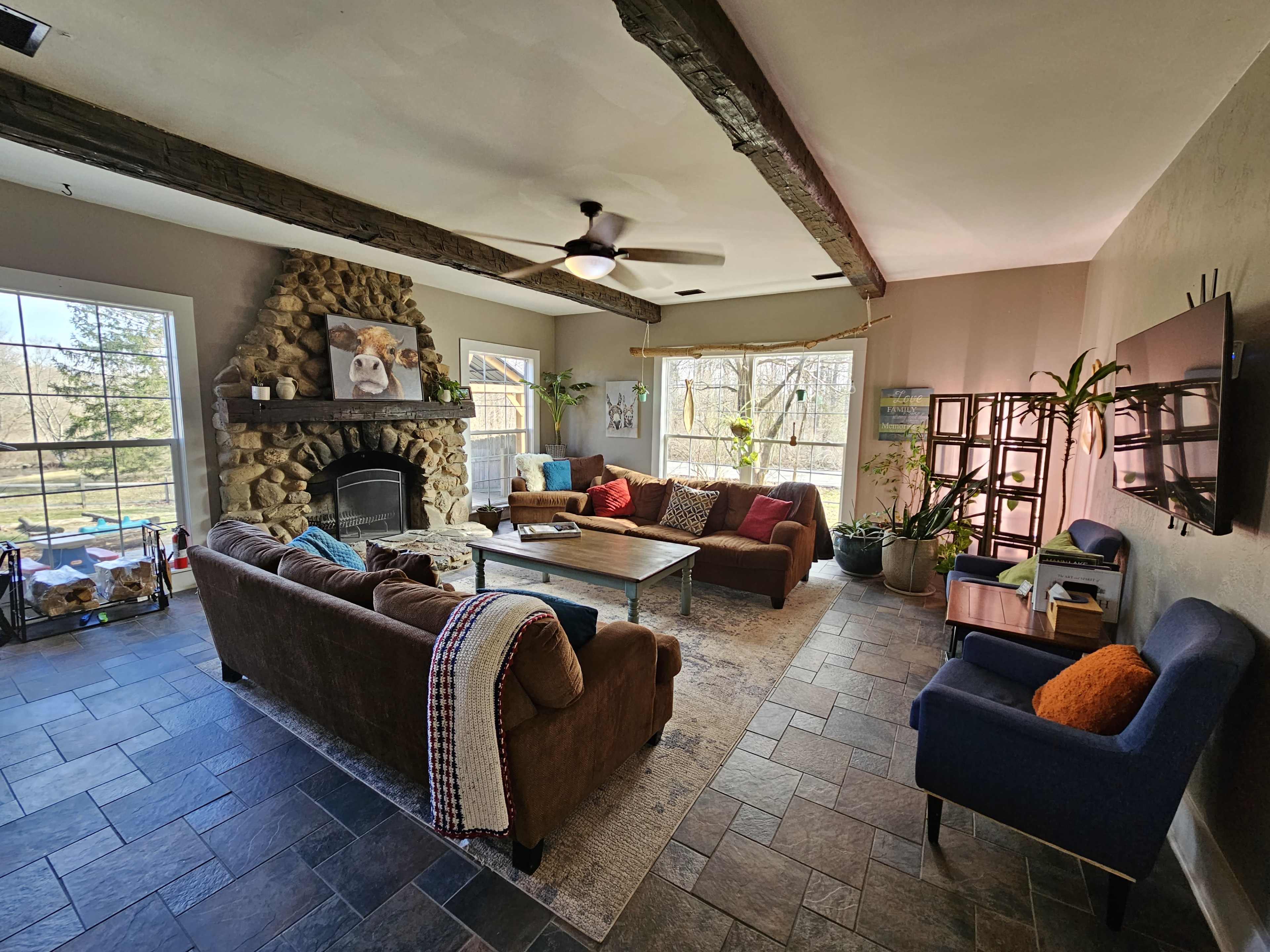 A spacious living room with a stone fireplace, two sofas, a coffee table, and large windows overlooking a wooded area.