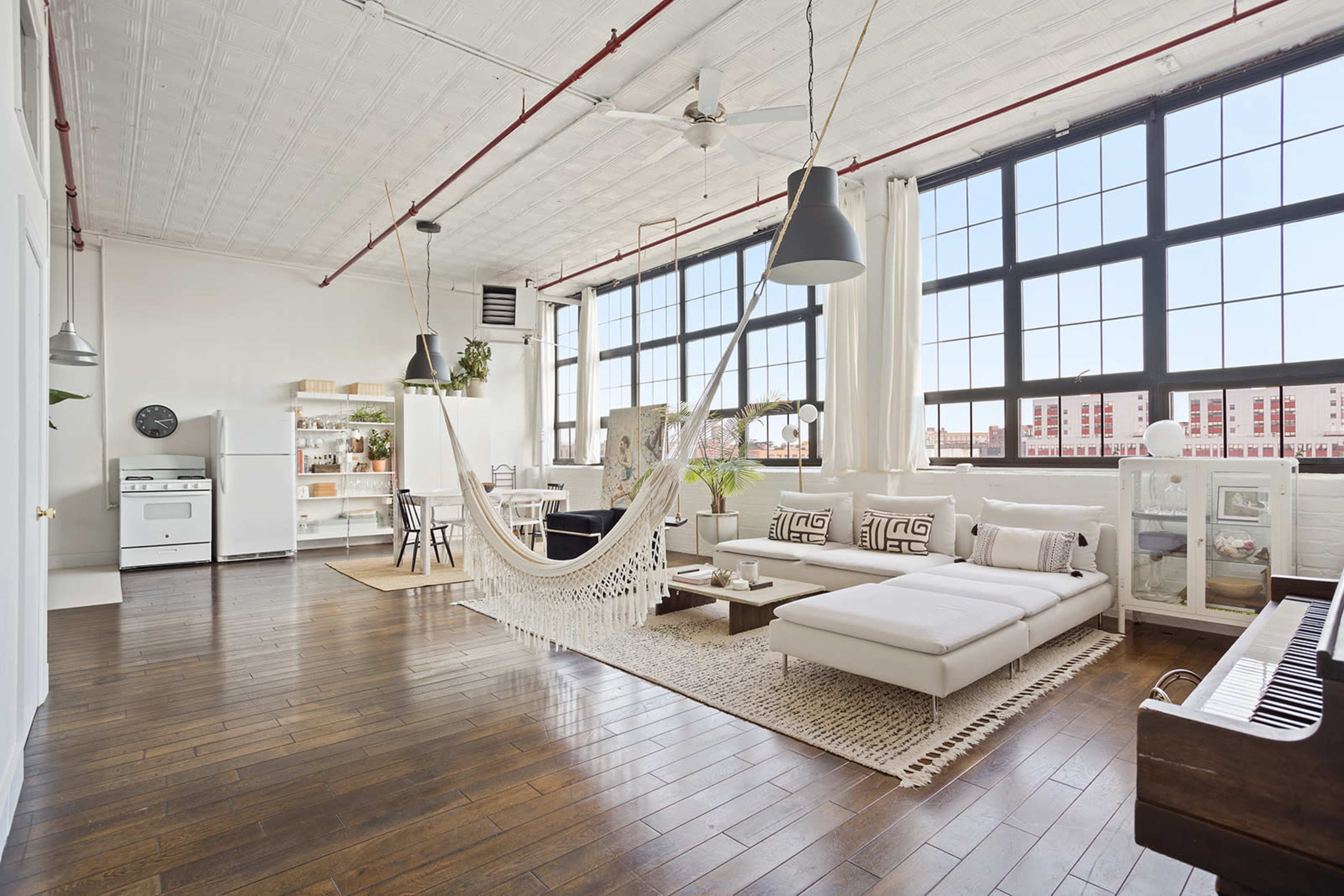 A spacious, well-lit loft with large windows, featuring a lounge area with a hammock and modern furniture.