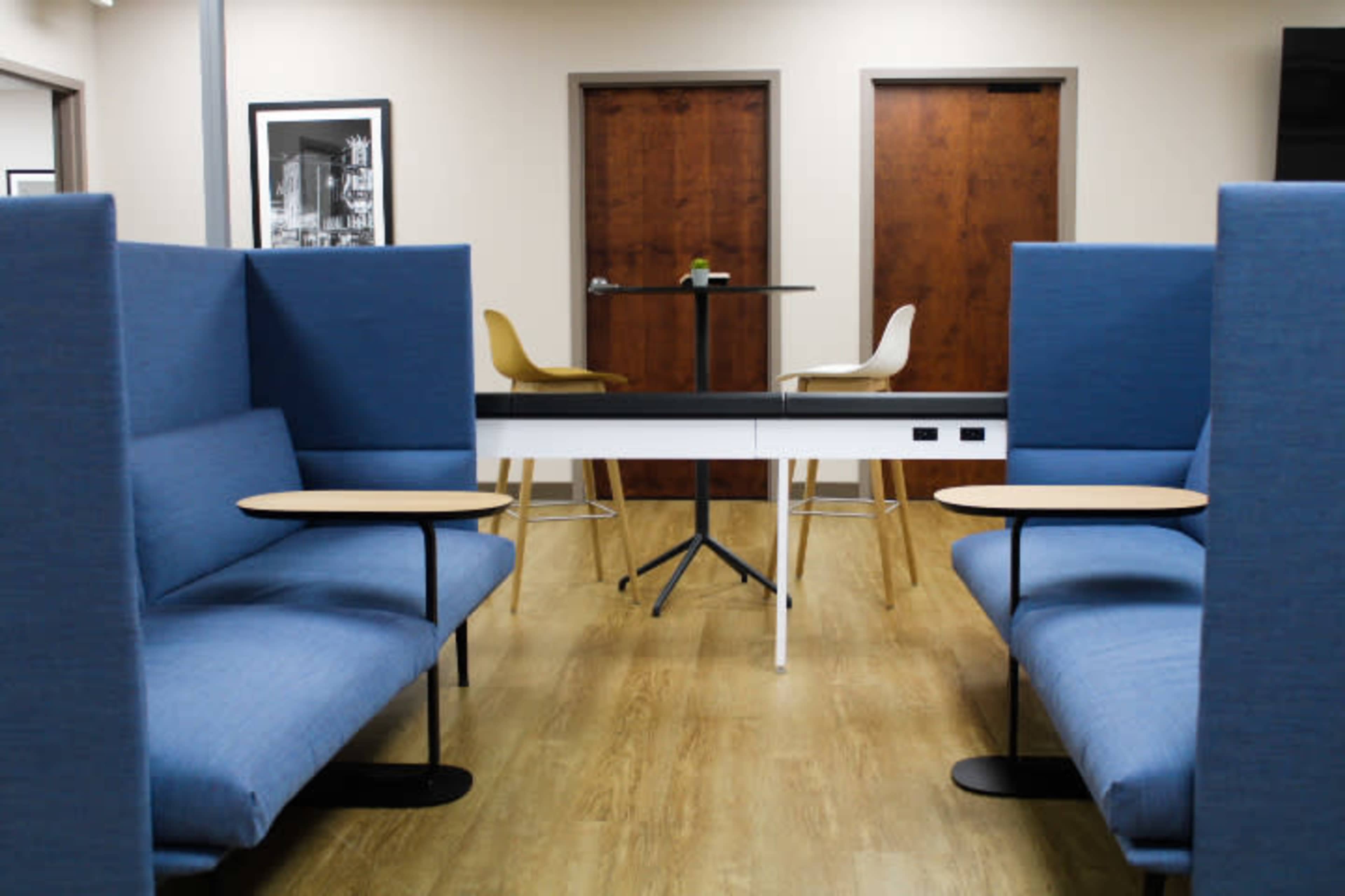 A lounge area with blue seating booths, a high table in the center, and two wooden doors in the background.