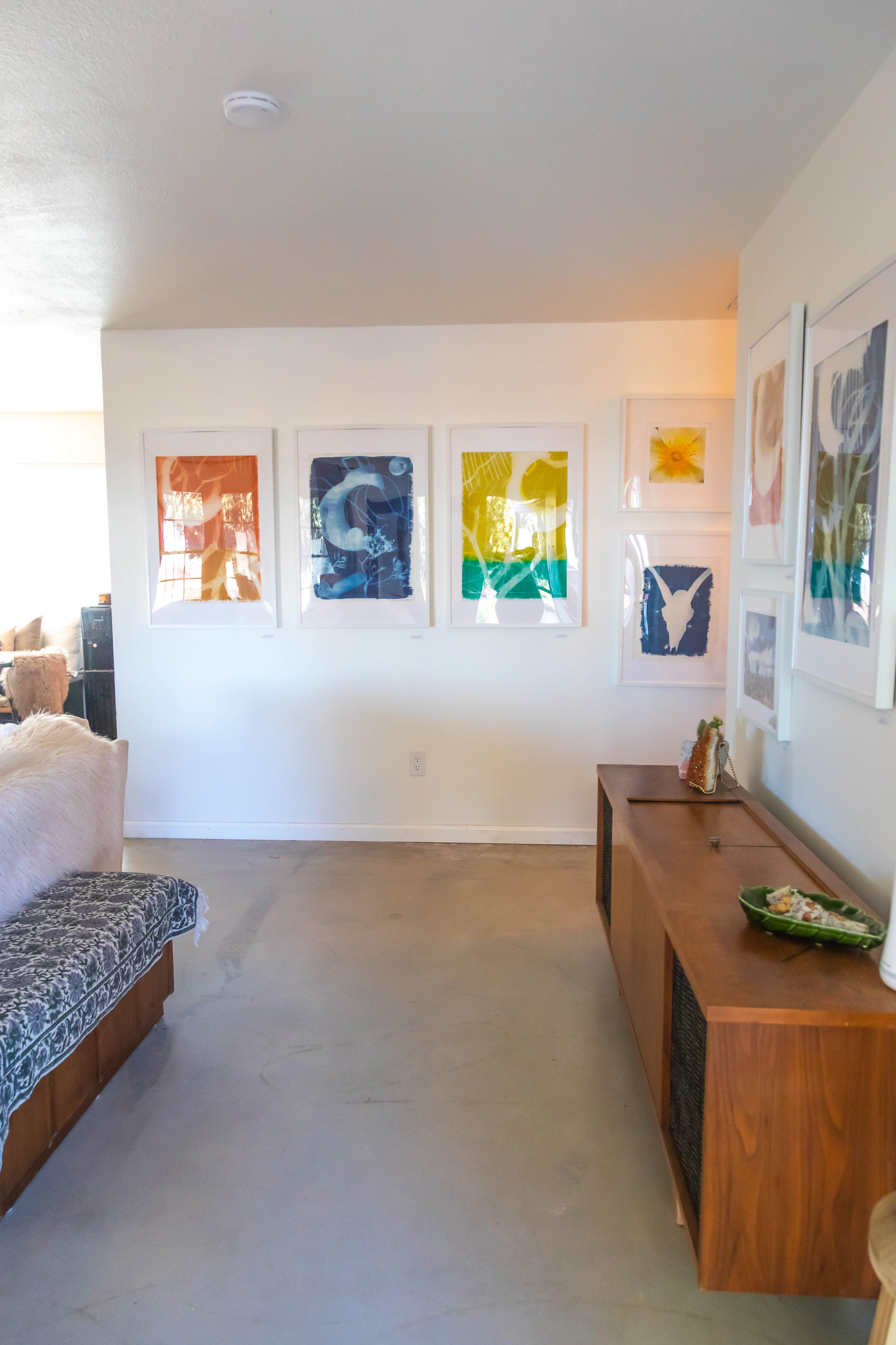 A modern living space with a minimalist sofa, a wooden media console, and a wall adorned with colorful framed artworks.