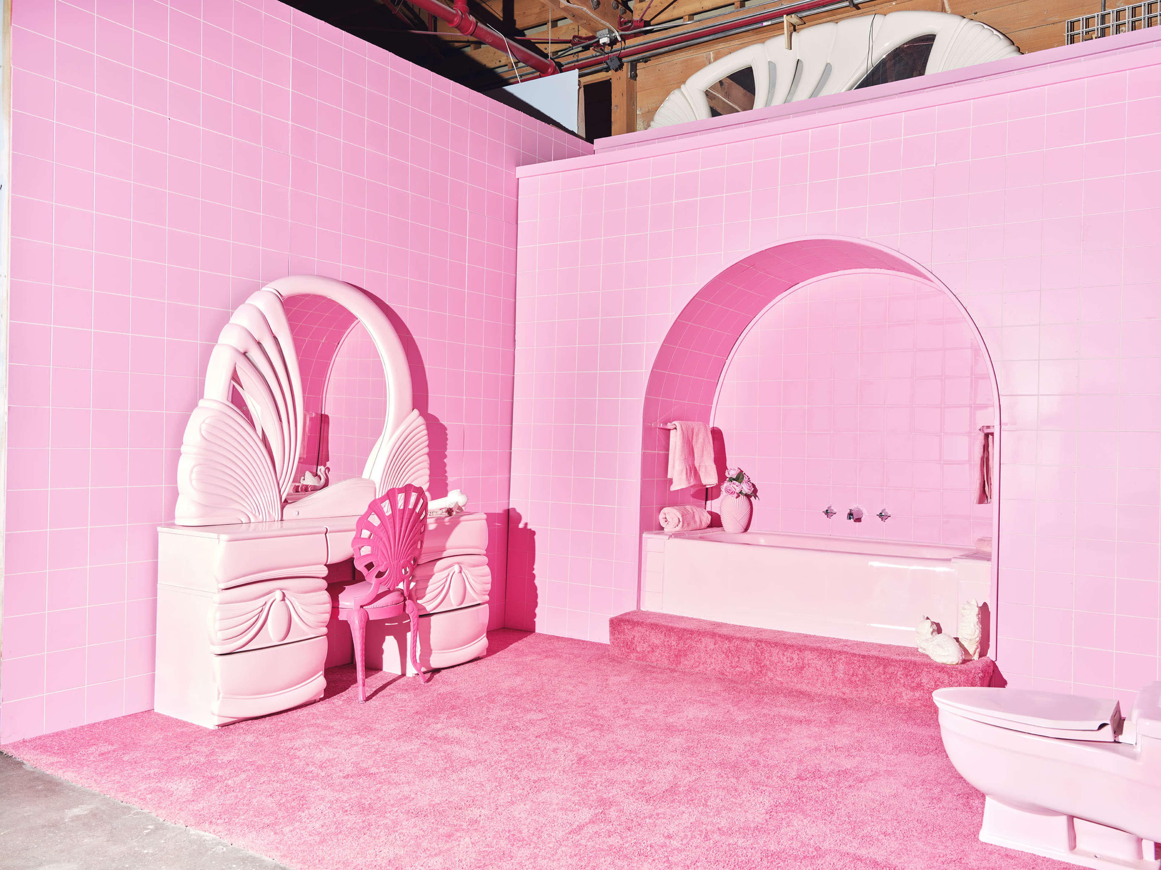 A pink bathroom featuring a bathtub, mirrors, a vanity, and a toilet, all set against bright pink tiled walls and carpet.