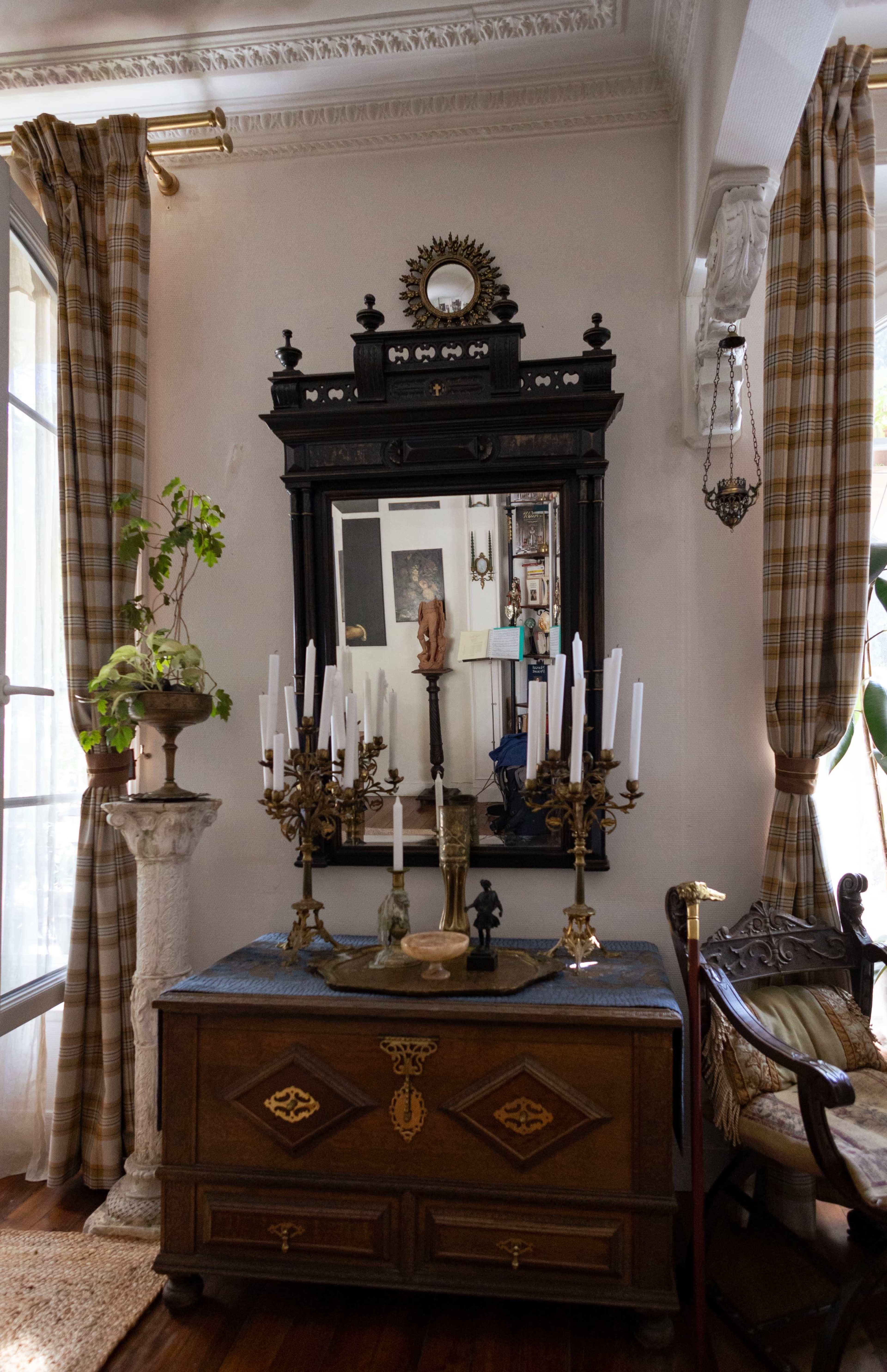 The scene features a vintage wooden dresser with decorative items, a large ornate mirror above it, and candles arranged on a candelabrum, set against a backdrop of curtains and a window.