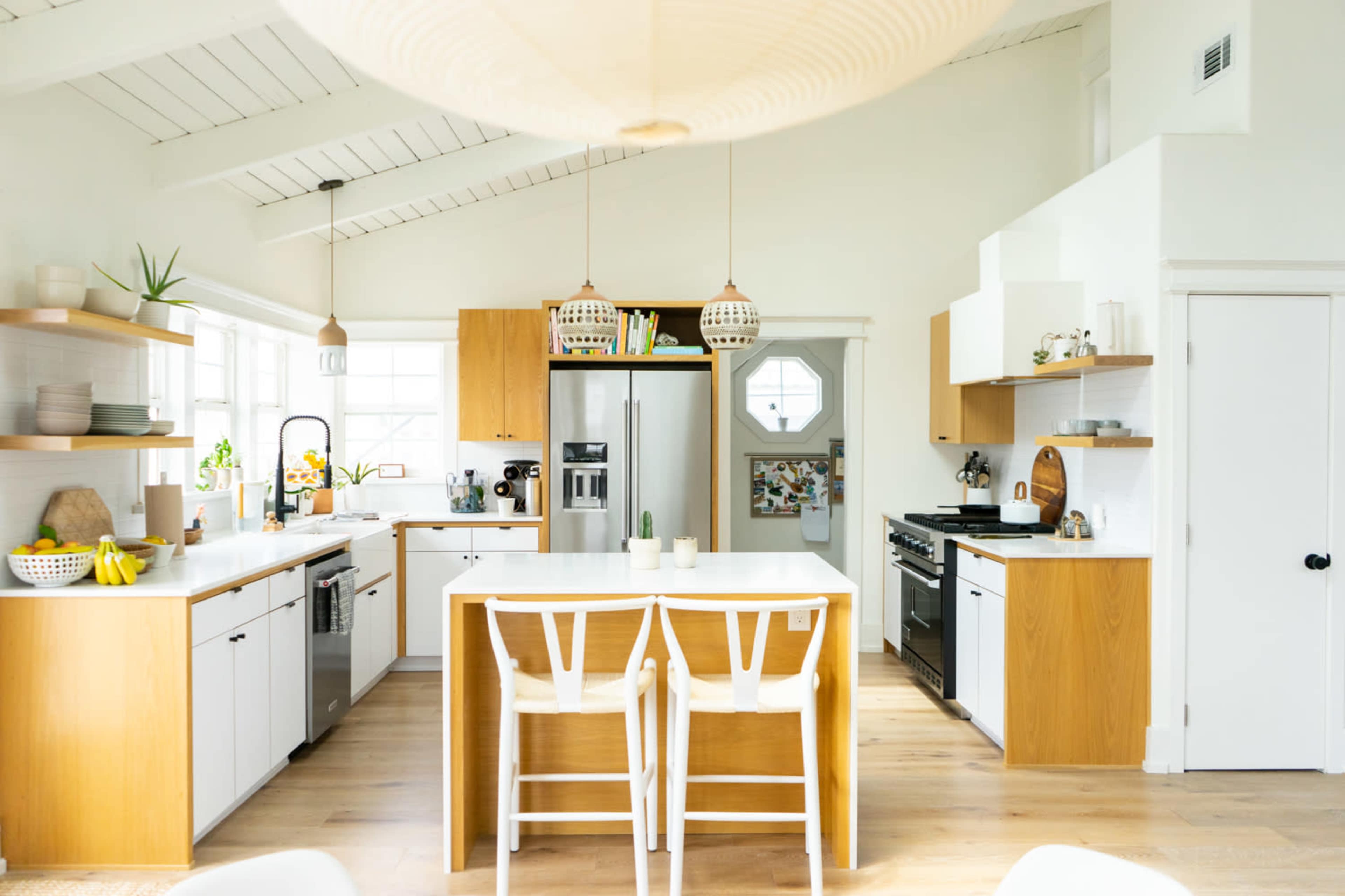 The kitchen features a modern design with wooden cabinets, stainless steel appliances, and a central island with white seating.