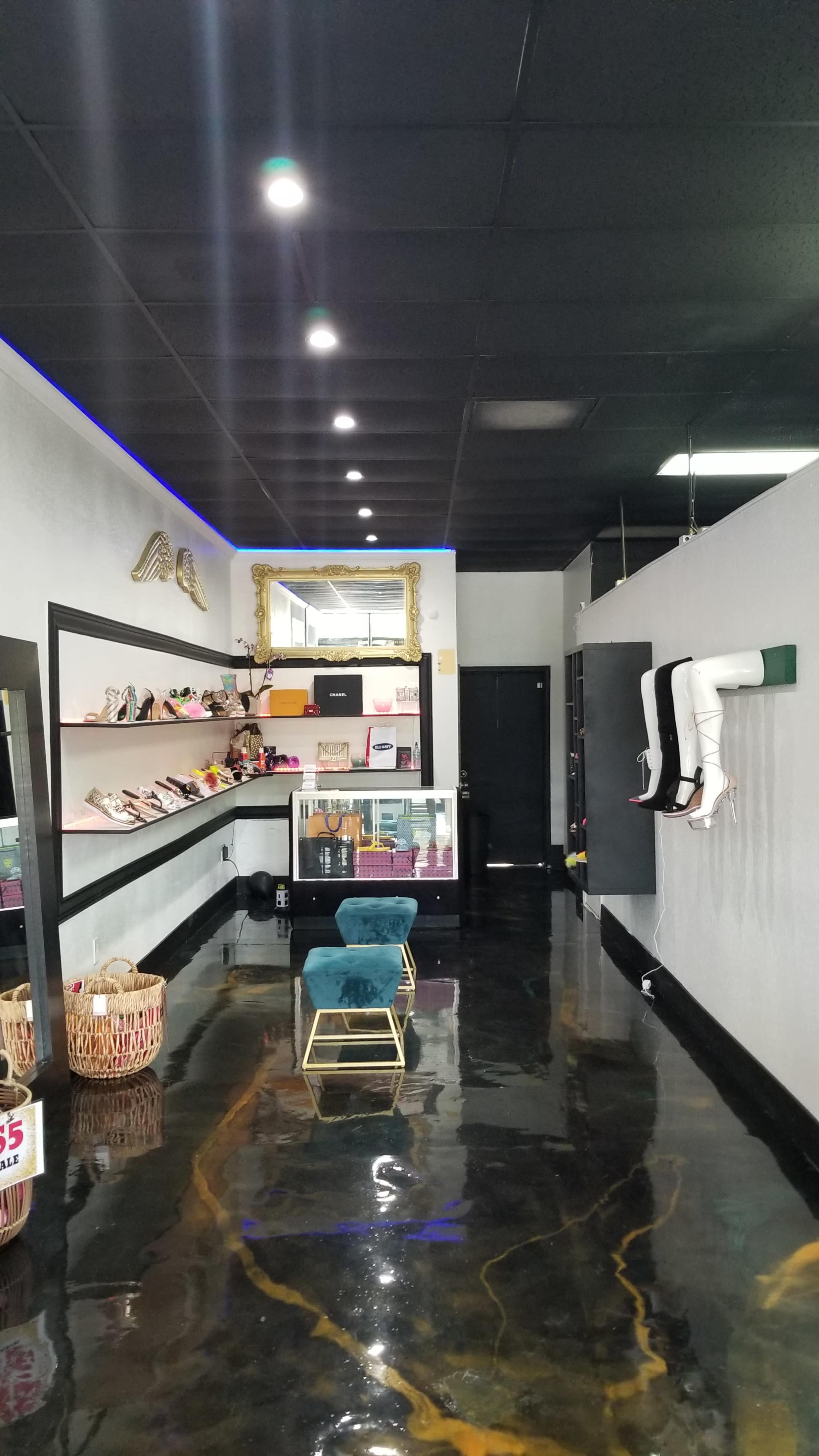 The interior of a boutique featuring shelves of shoes, a display case, a stylish chair, and a decorative mirror along a polished floor.