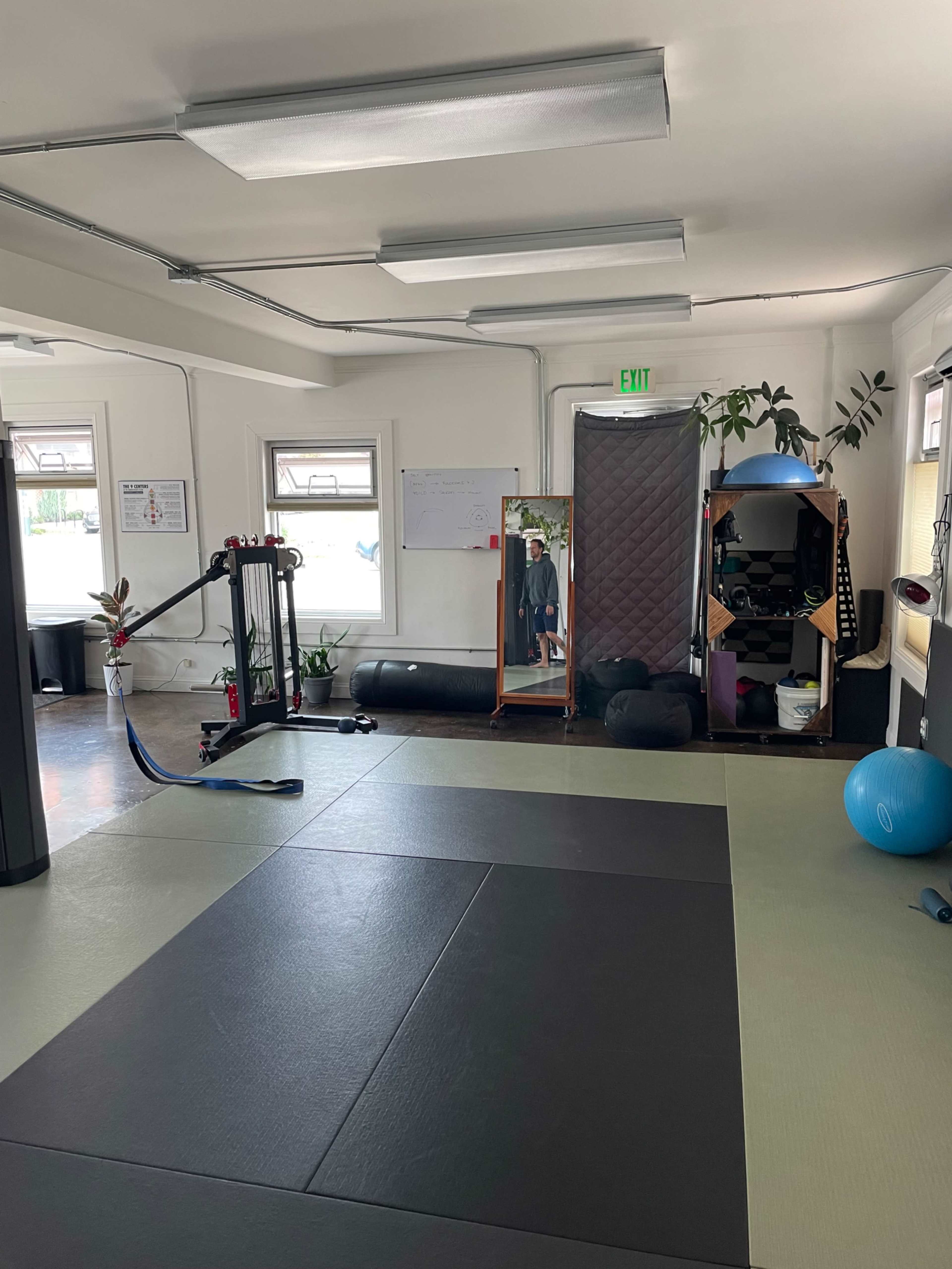 The image shows an indoor space designed for physical activities, featuring exercise mats, fitness equipment, mirrors, and a large exercise ball.
