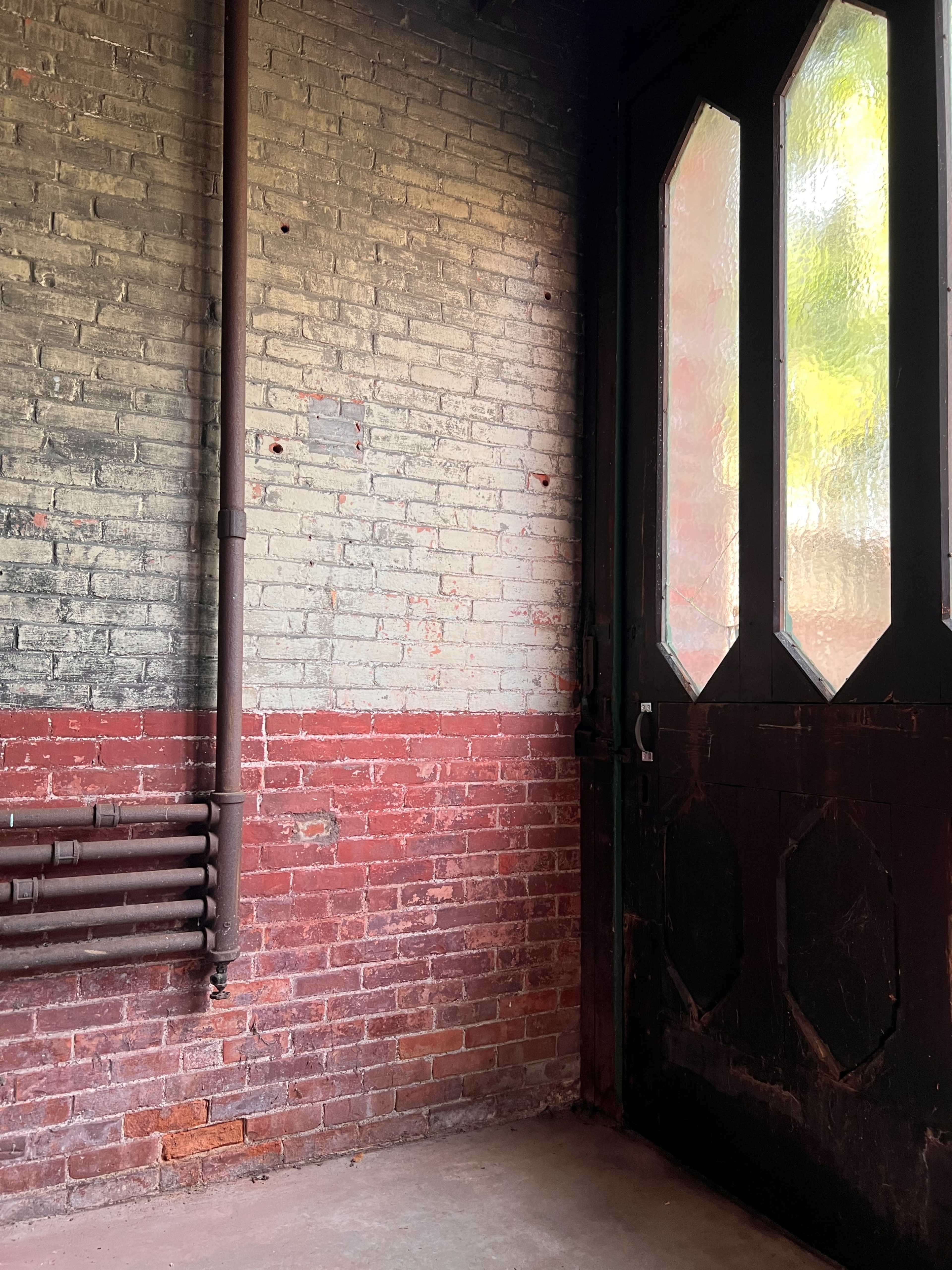 The image shows a corner of a room with a brick wall painted in two colors, red and gray, featuring a textured glass door.