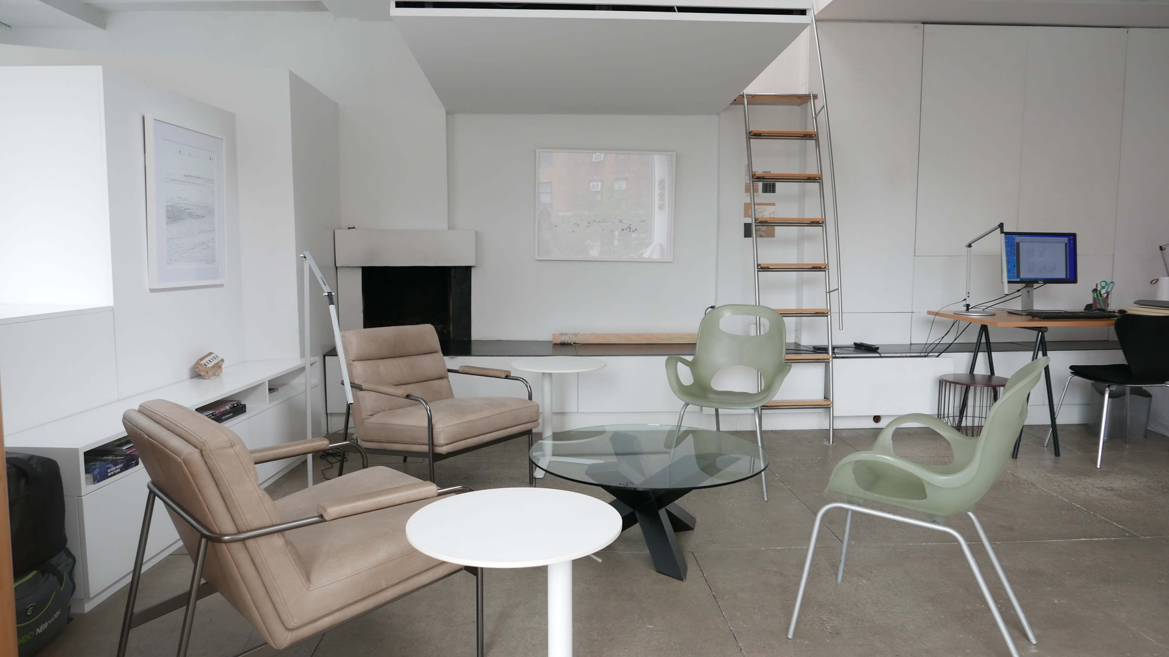 A modern interior space featuring two armchairs, a circular glass coffee table, a small white table, and a staircase leading to an upper level, with a minimalist design throughout.