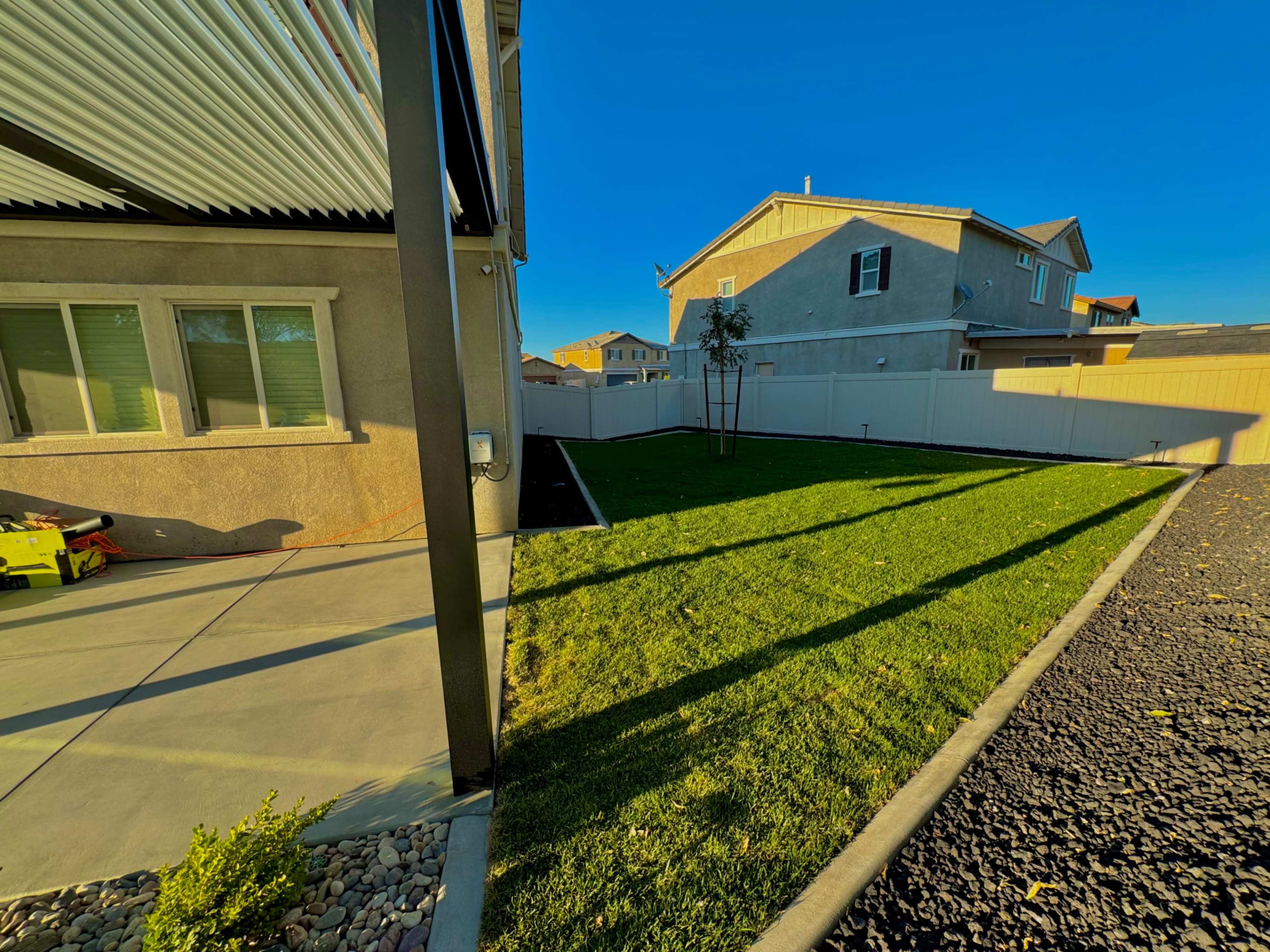 A well-maintained yard with a grassy area bordered by a fence and a concrete patio beside a house.