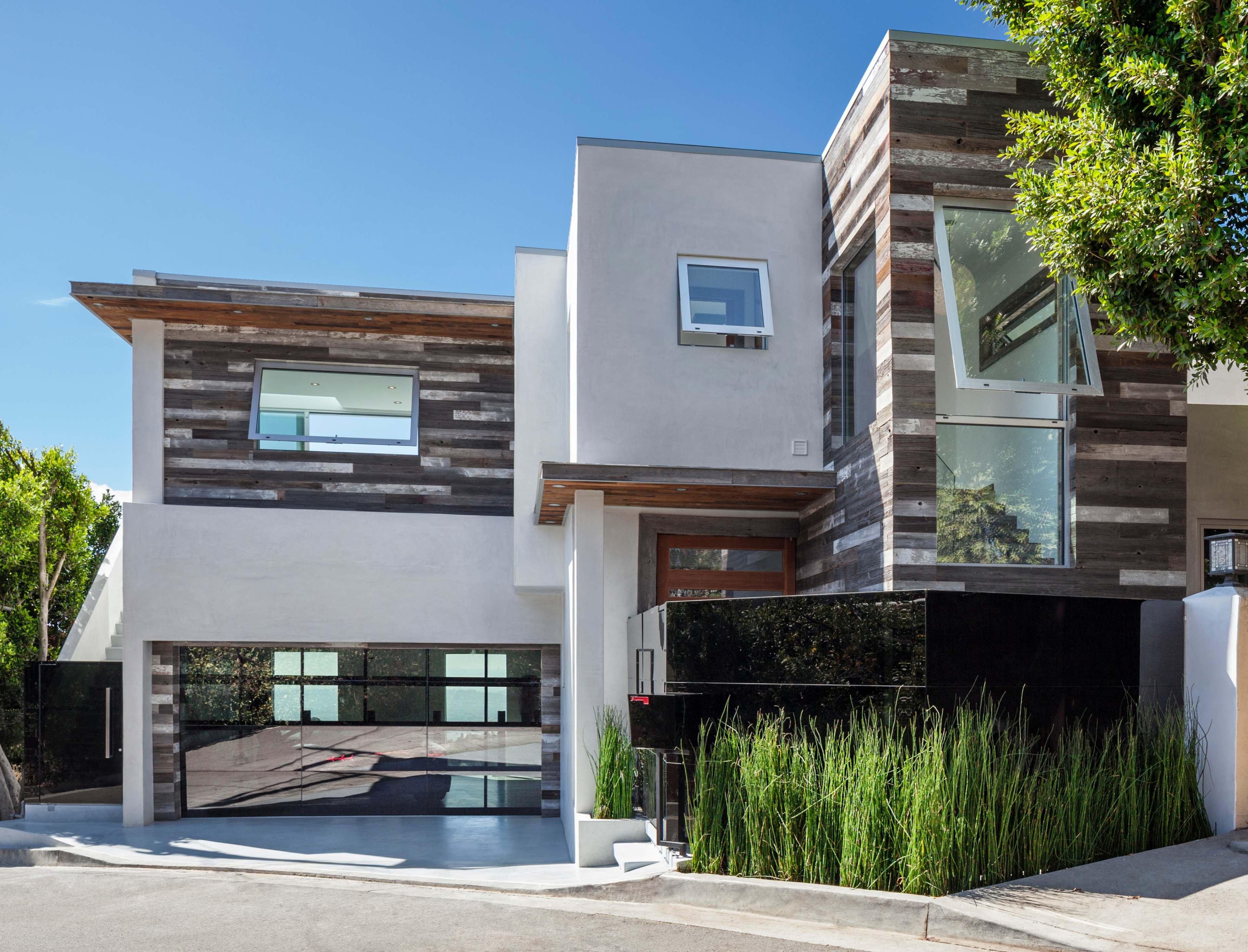 A modern two-story house featuring a combination of textured wood and sleek black materials, with large windows and a garage.