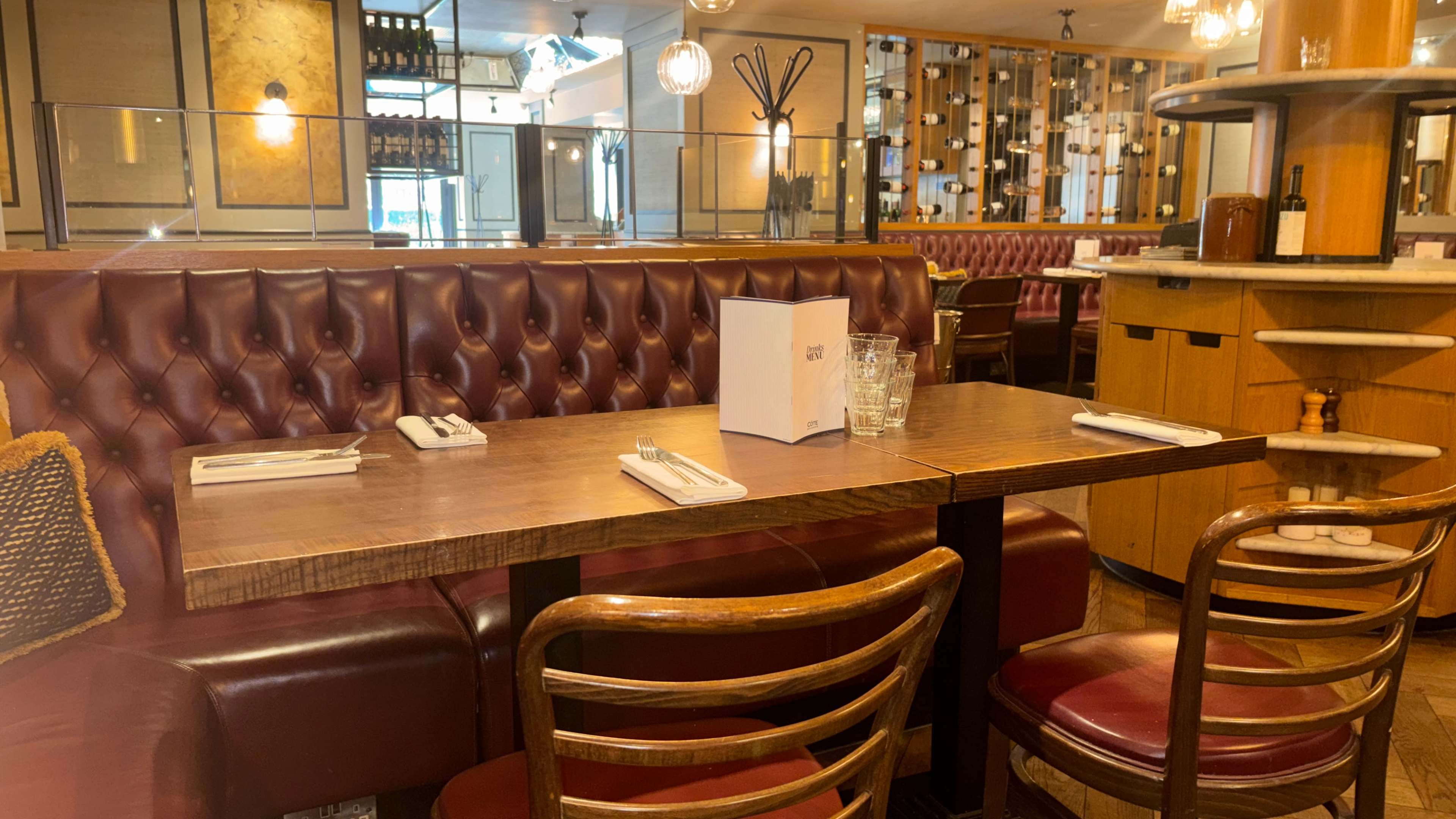 The image shows a table set for dining in a restaurant with upholstered seating and a modern decor.