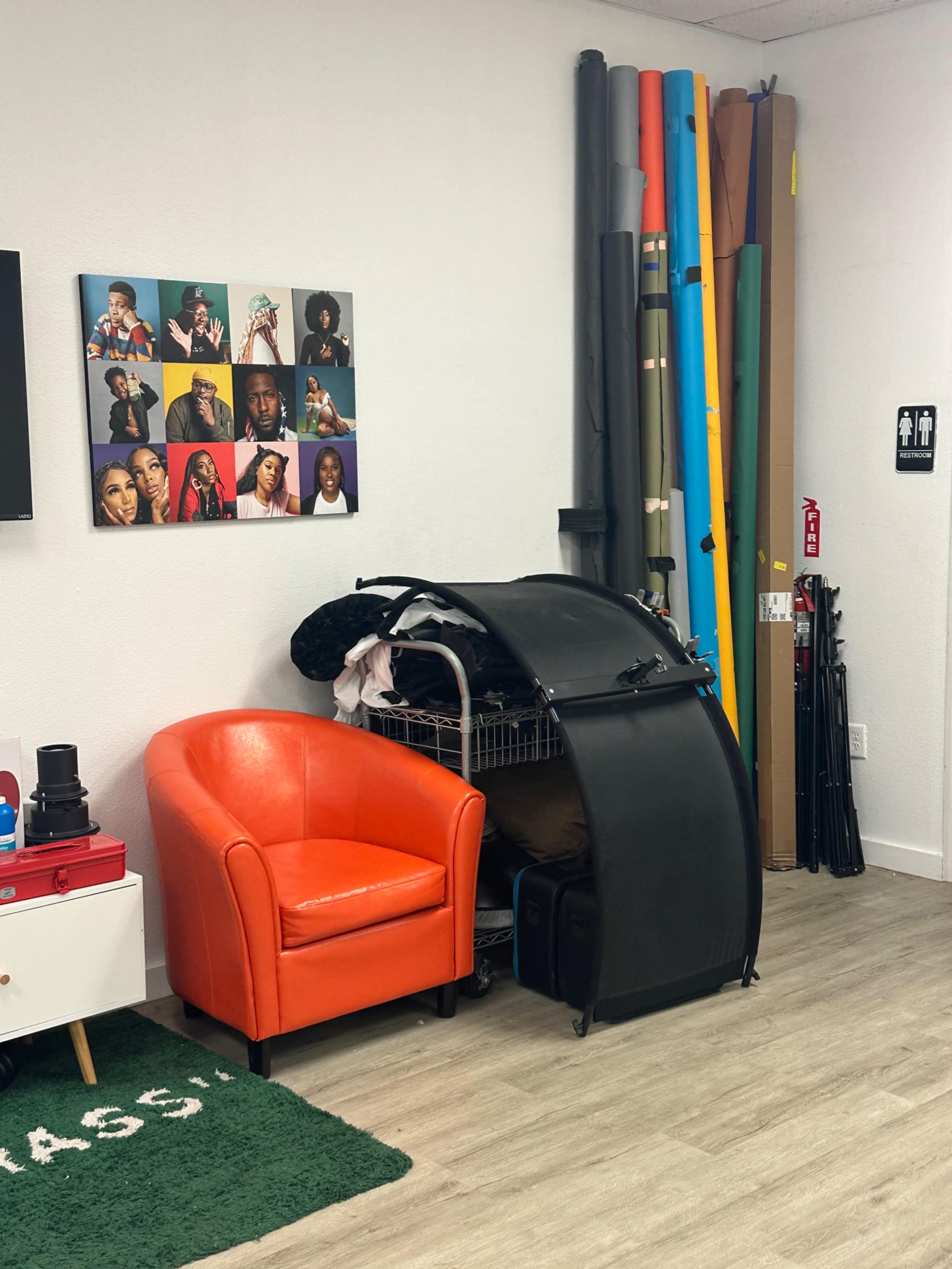 An orange armchair next to a rack with various props and backdrop rolls in a studio space.