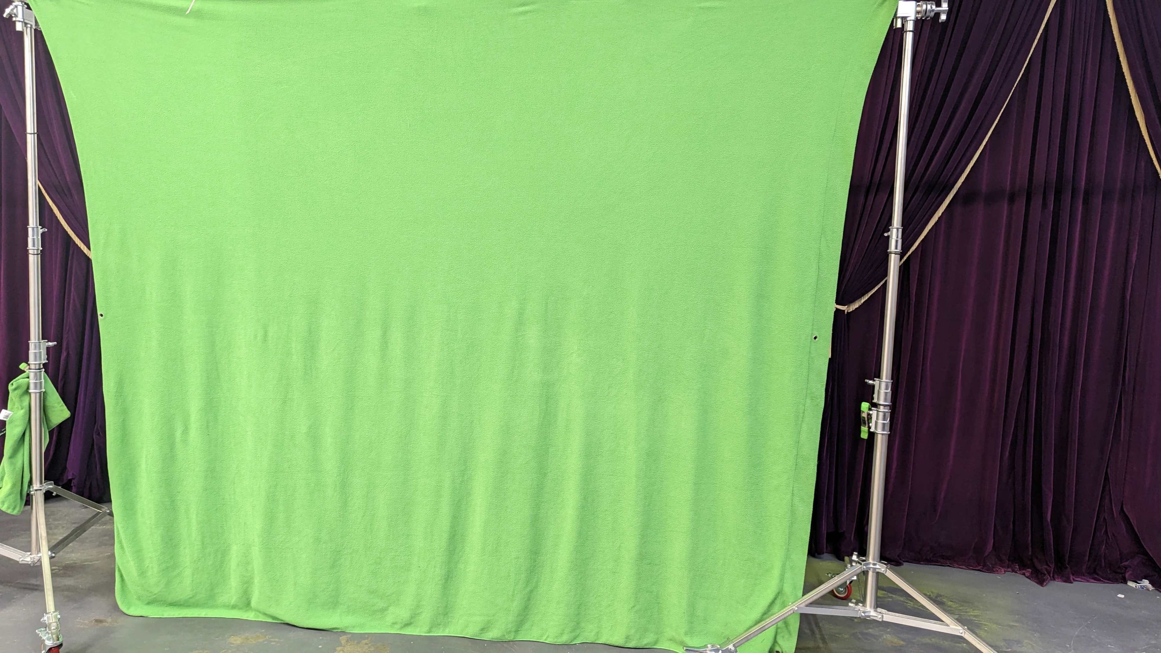 A green screen setup on a metal frame in front of a dark curtain backdrop.