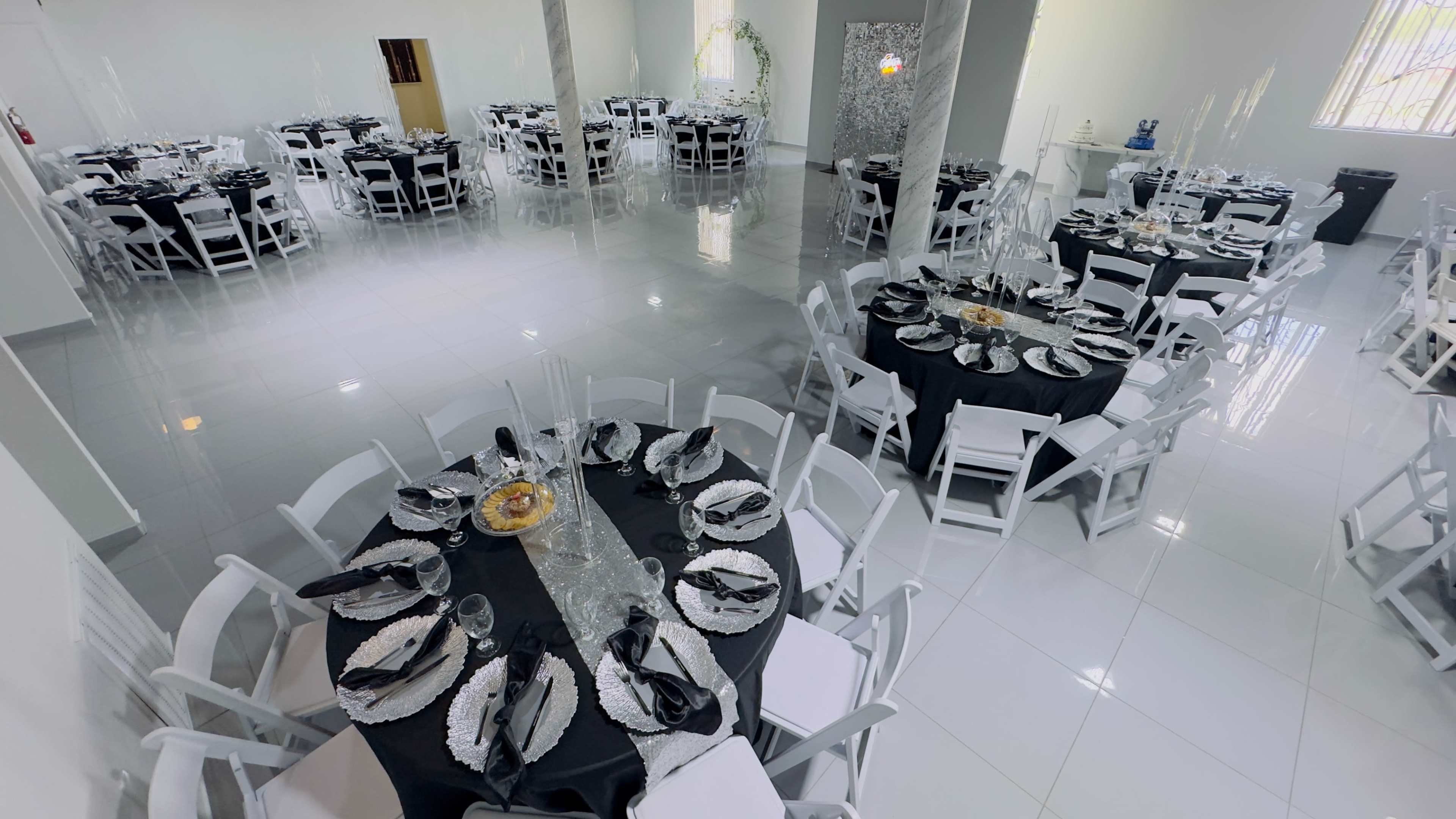 The image shows a spacious event hall set up with several round tables covered in black and white tablecloths, arranged for a formal dining experience.