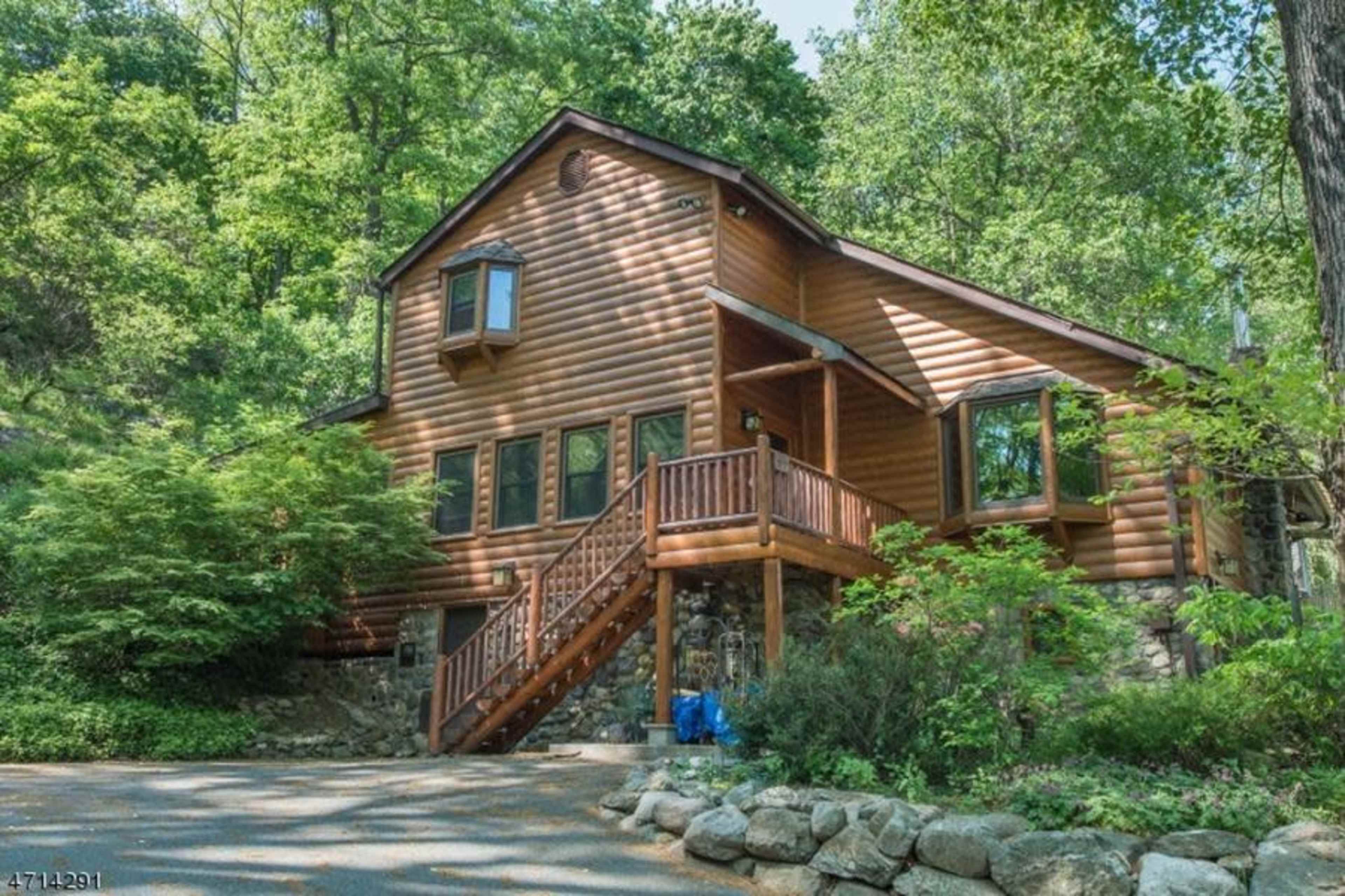 A two-story wooden cabin nestled among lush green trees, featuring a front porch and stone accents.