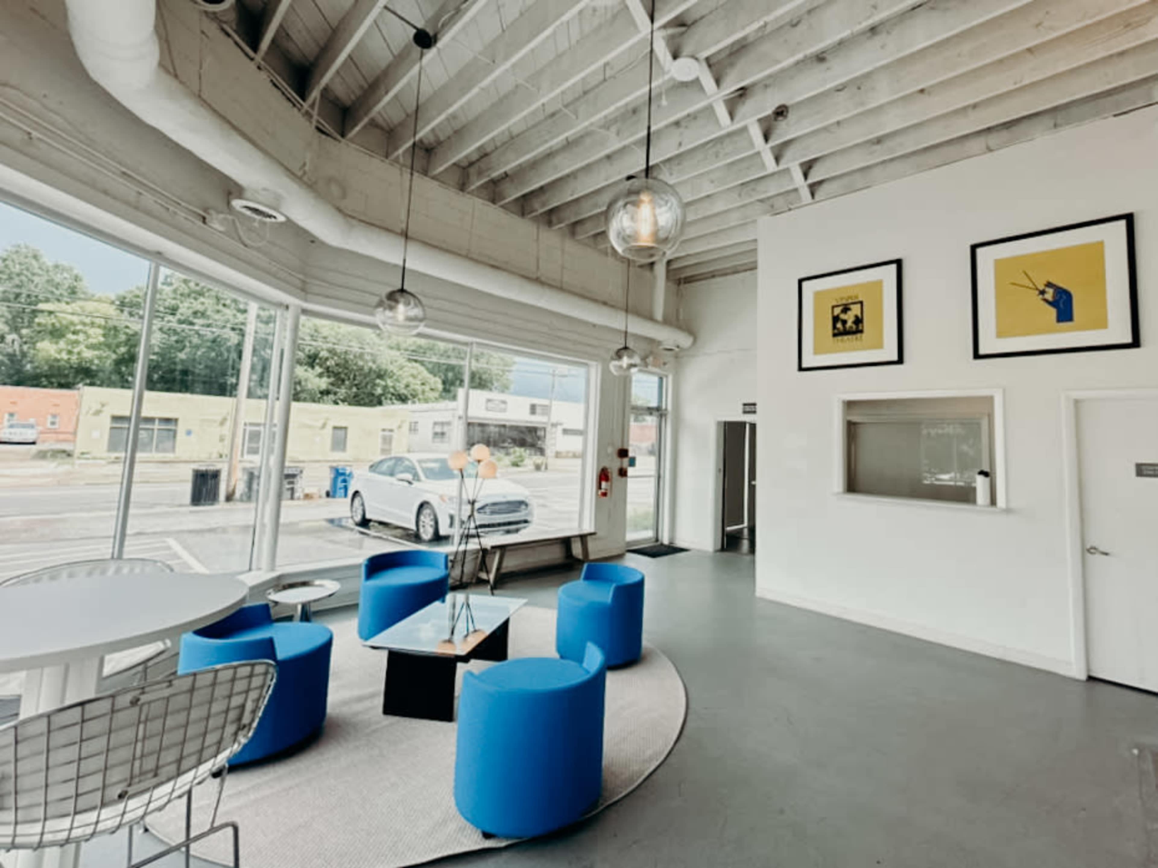 The image shows a modern, well-lit reception area with blue seating, a round table, and large windows allowing natural light to enter.