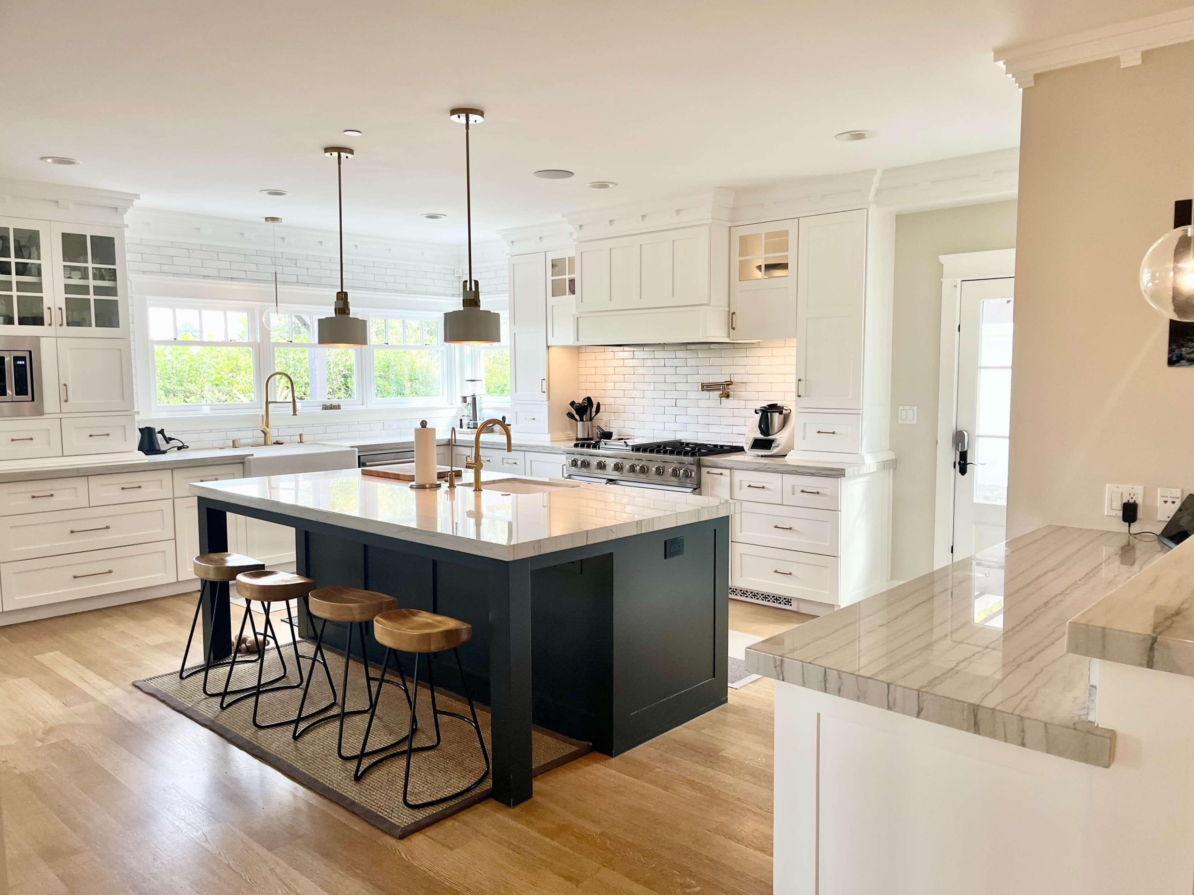 The image shows a modern kitchen featuring white cabinetry, a large central island with bar stools, and stainless steel appliances.