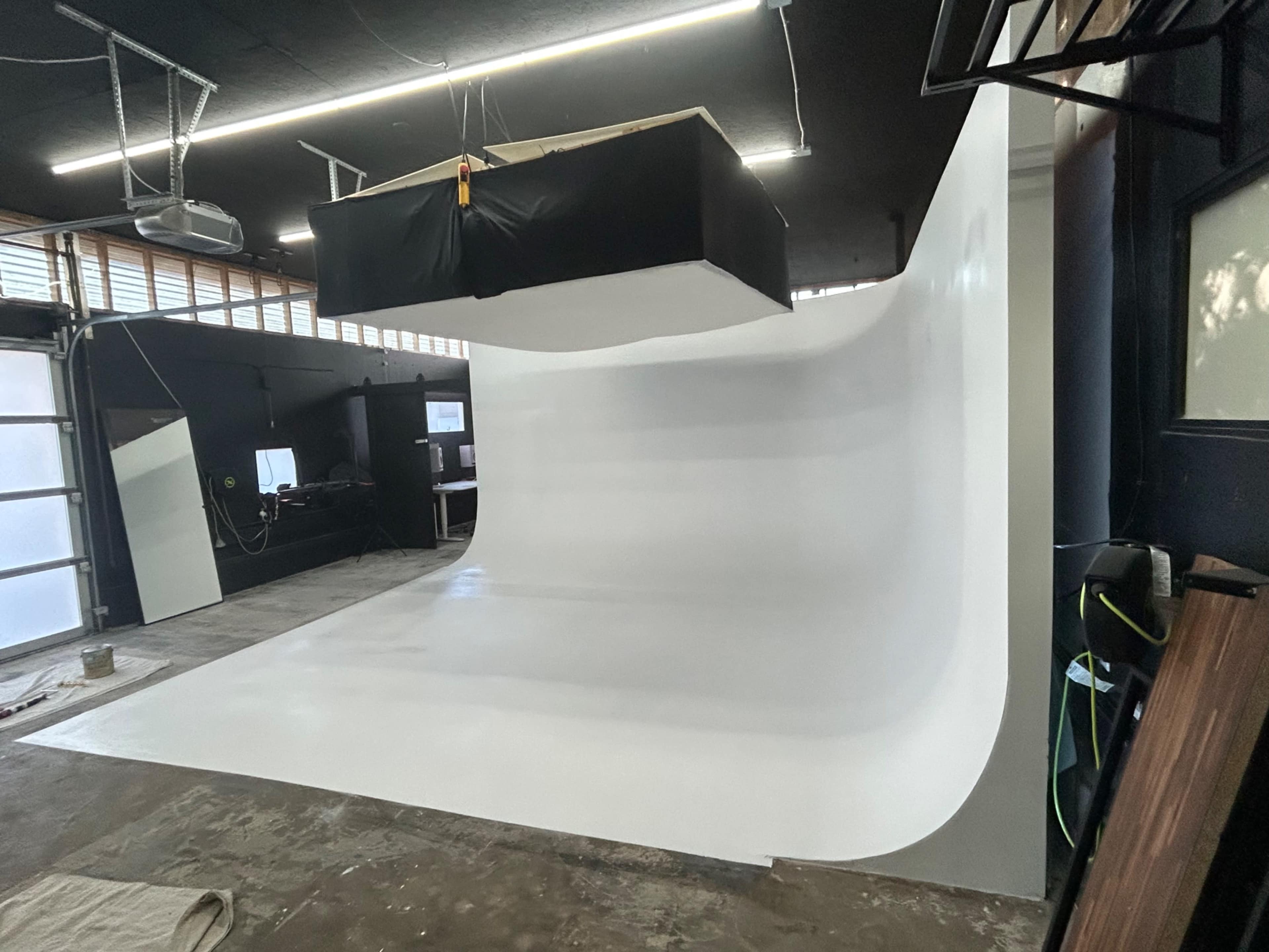 The image shows a large, empty studio space with a seamless white backdrop and a suspended lighting setup.
