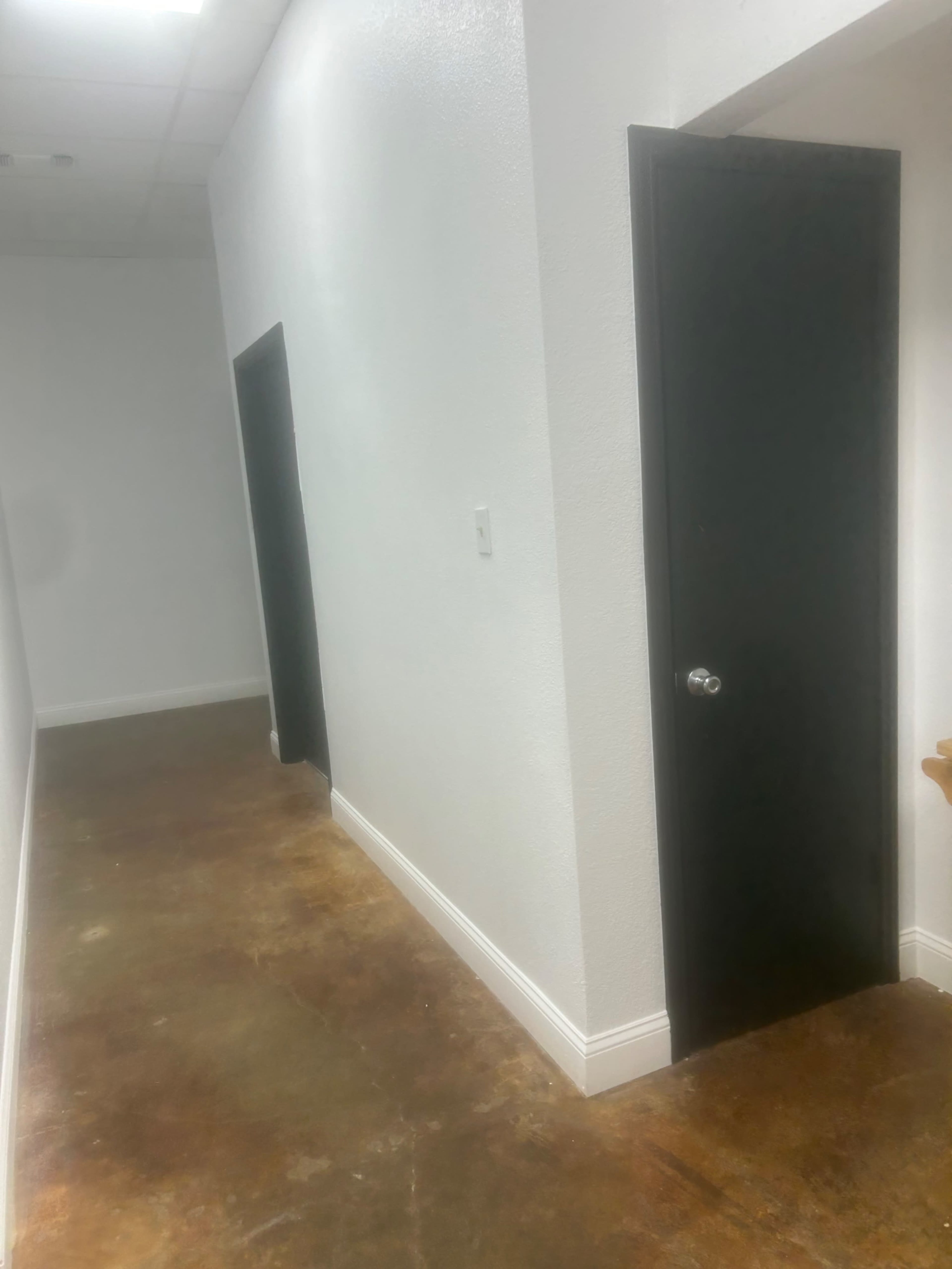 The image shows a narrow hallway with a concrete floor and two black doors on opposite walls.