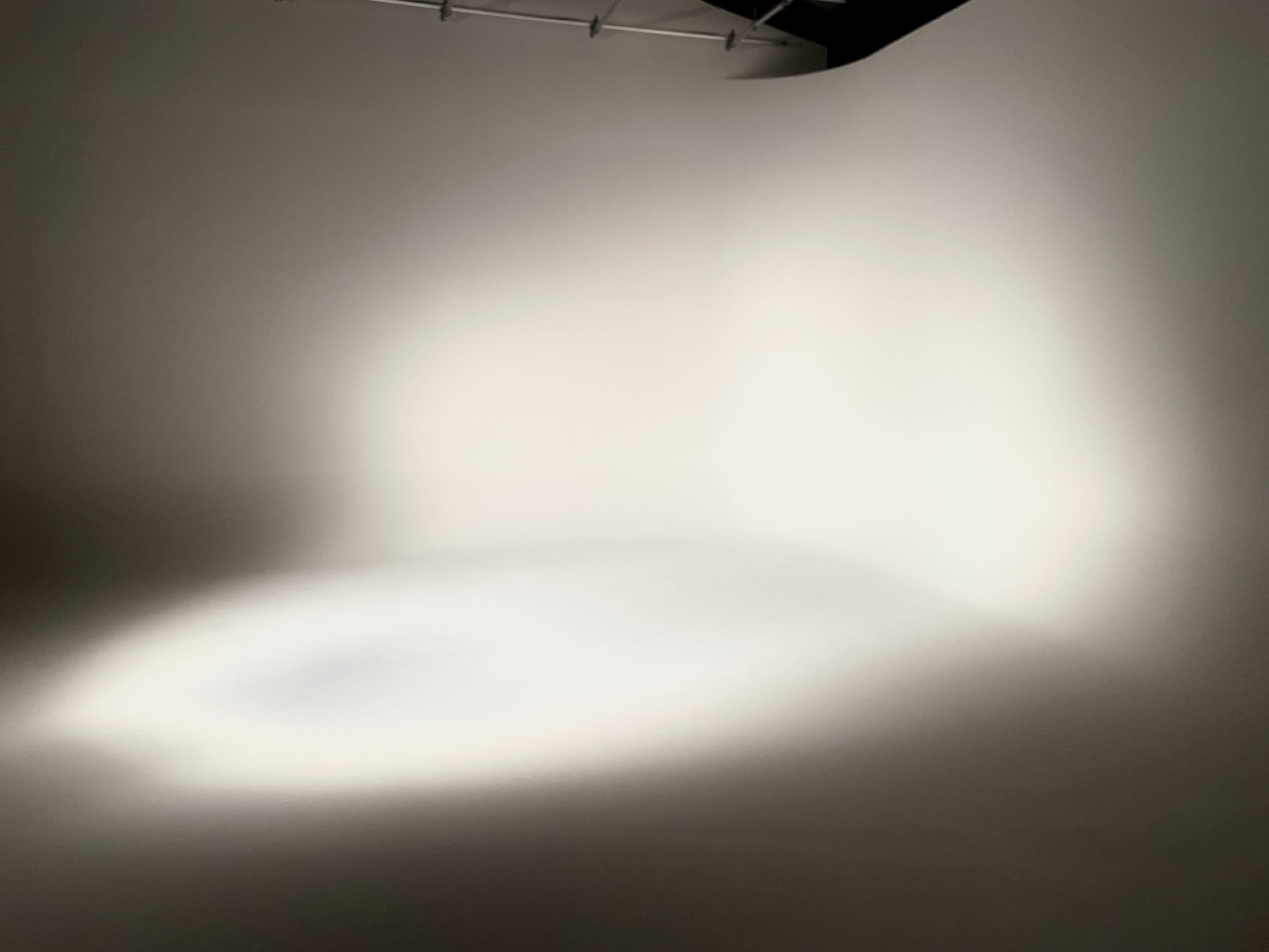 A softly lit studio space with a plain, light-colored background and a subtle light gradient on the floor.