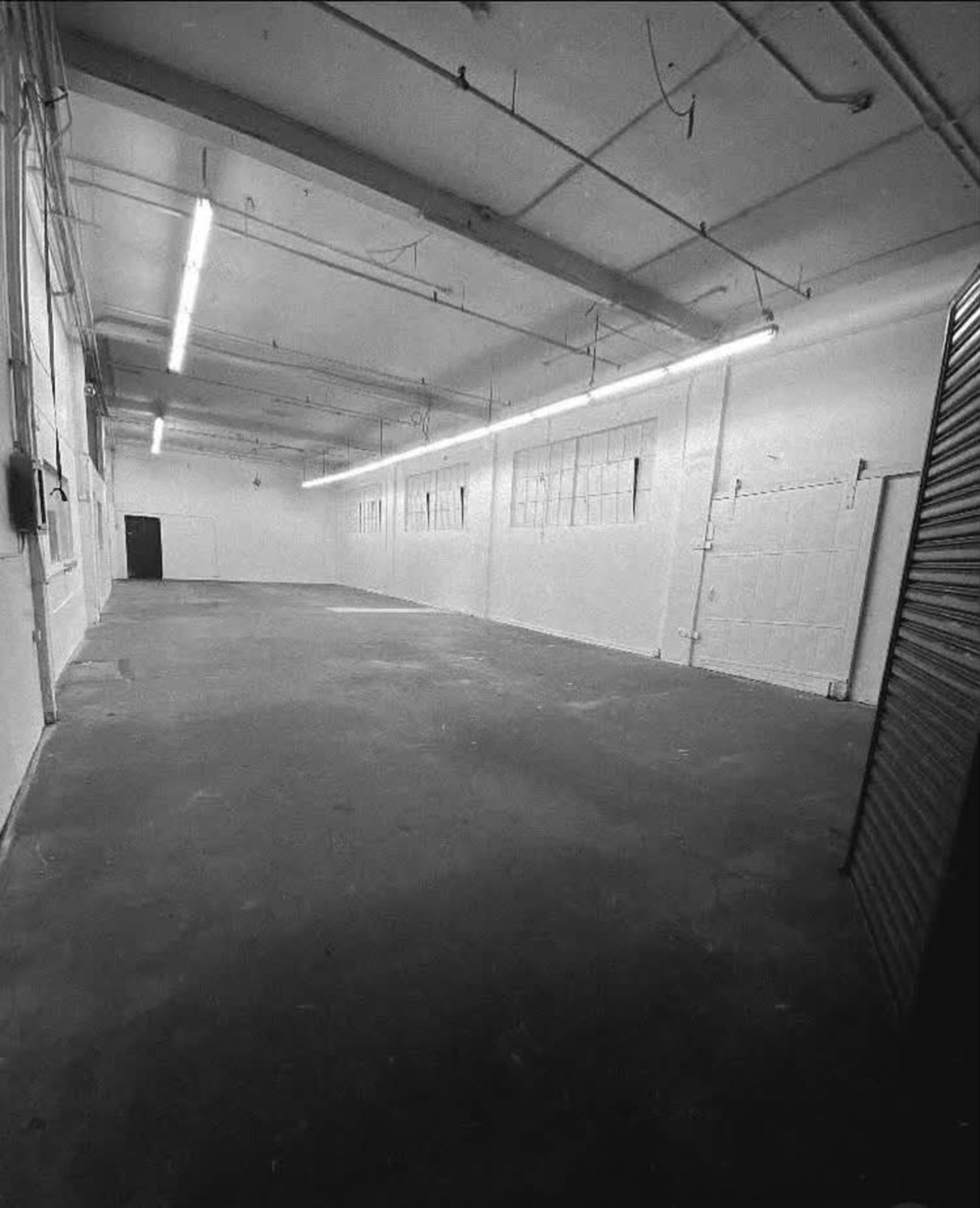 The image shows a large, empty industrial warehouse space with concrete flooring and overhead lighting.