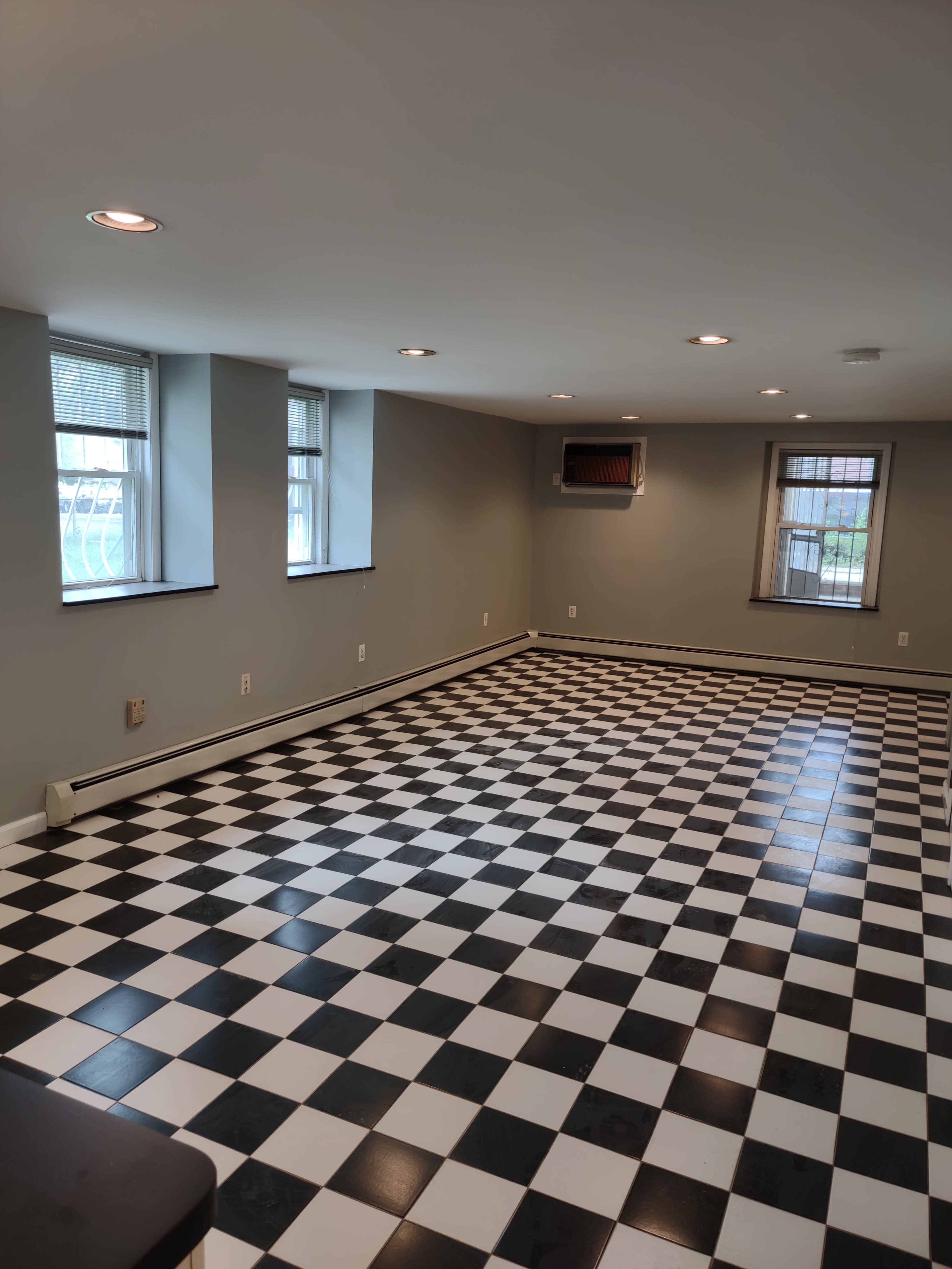 A spacious room with black and white checkered tiles, two windows, and a wall-mounted air conditioning unit.