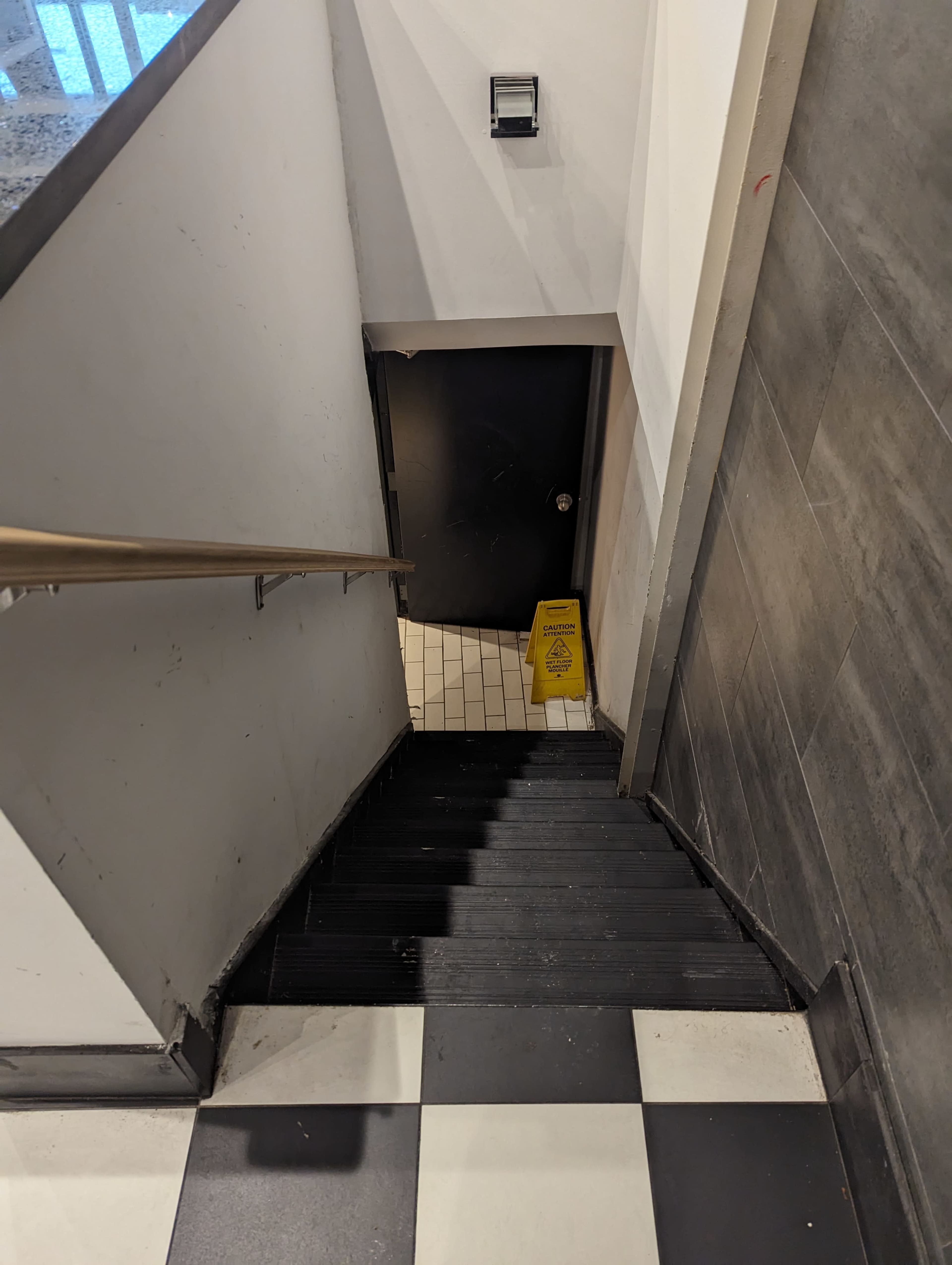 A staircase leads down to a door at the bottom, with a caution sign placed on the landing.