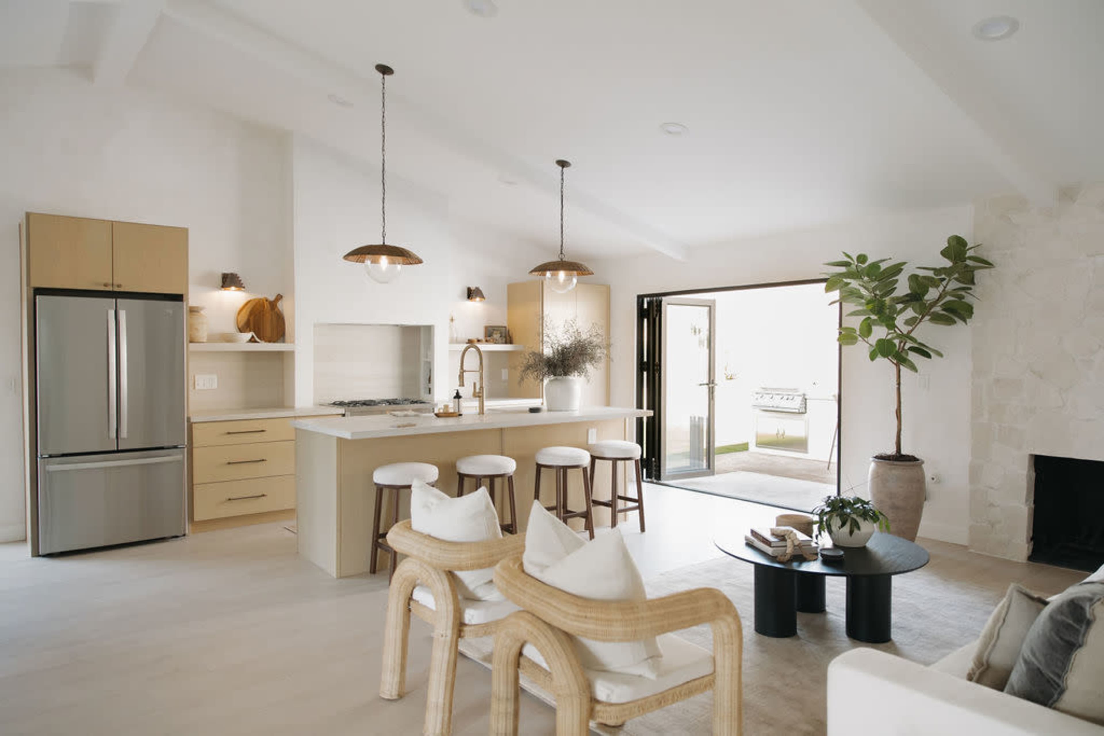 A modern kitchen with a bar, light wood cabinetry, and a seating area that opens to an outdoor space.