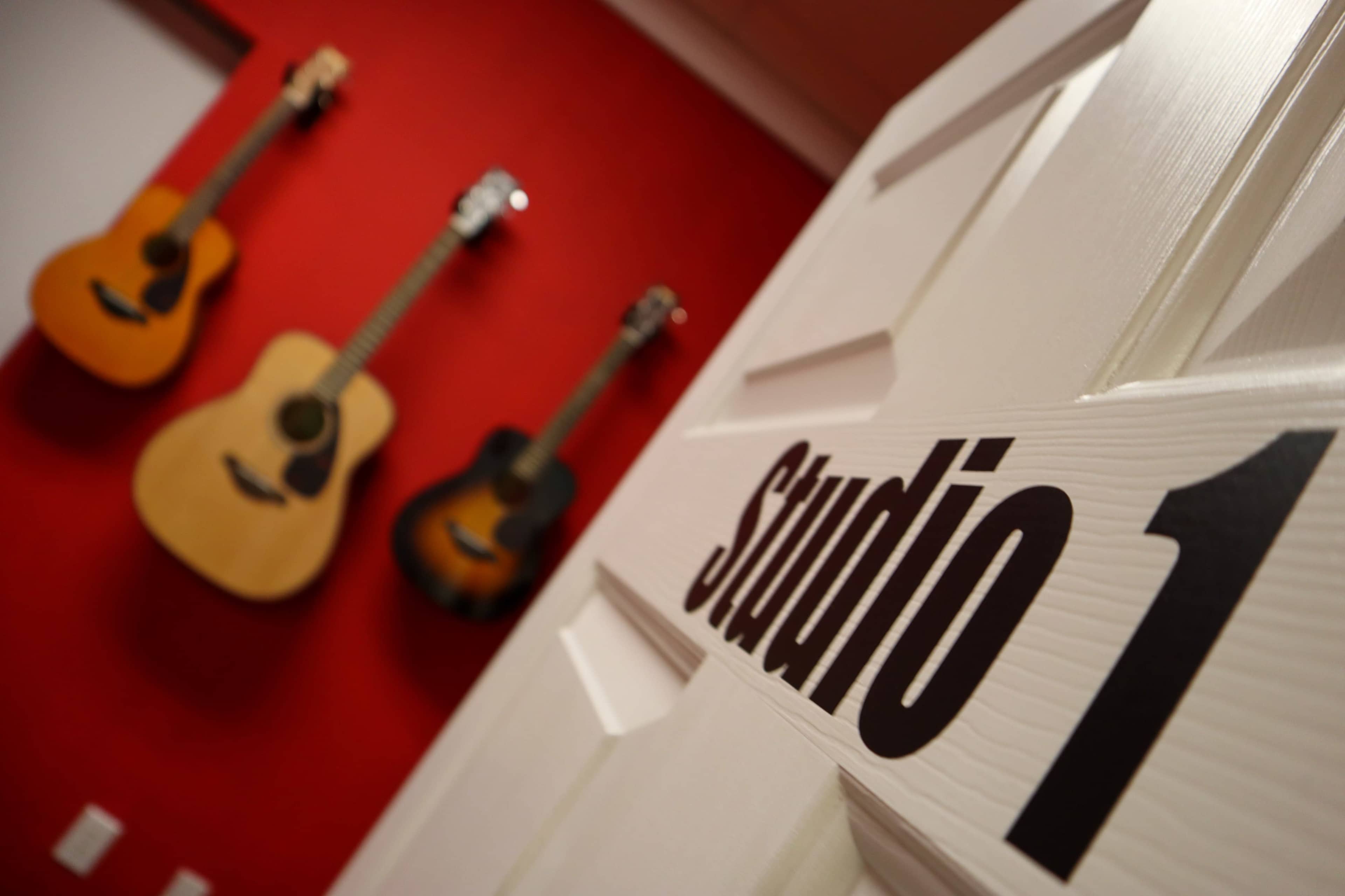 A white door labeled "Studio 1" is shown in the foreground, with three guitars mounted on a red wall in the background.