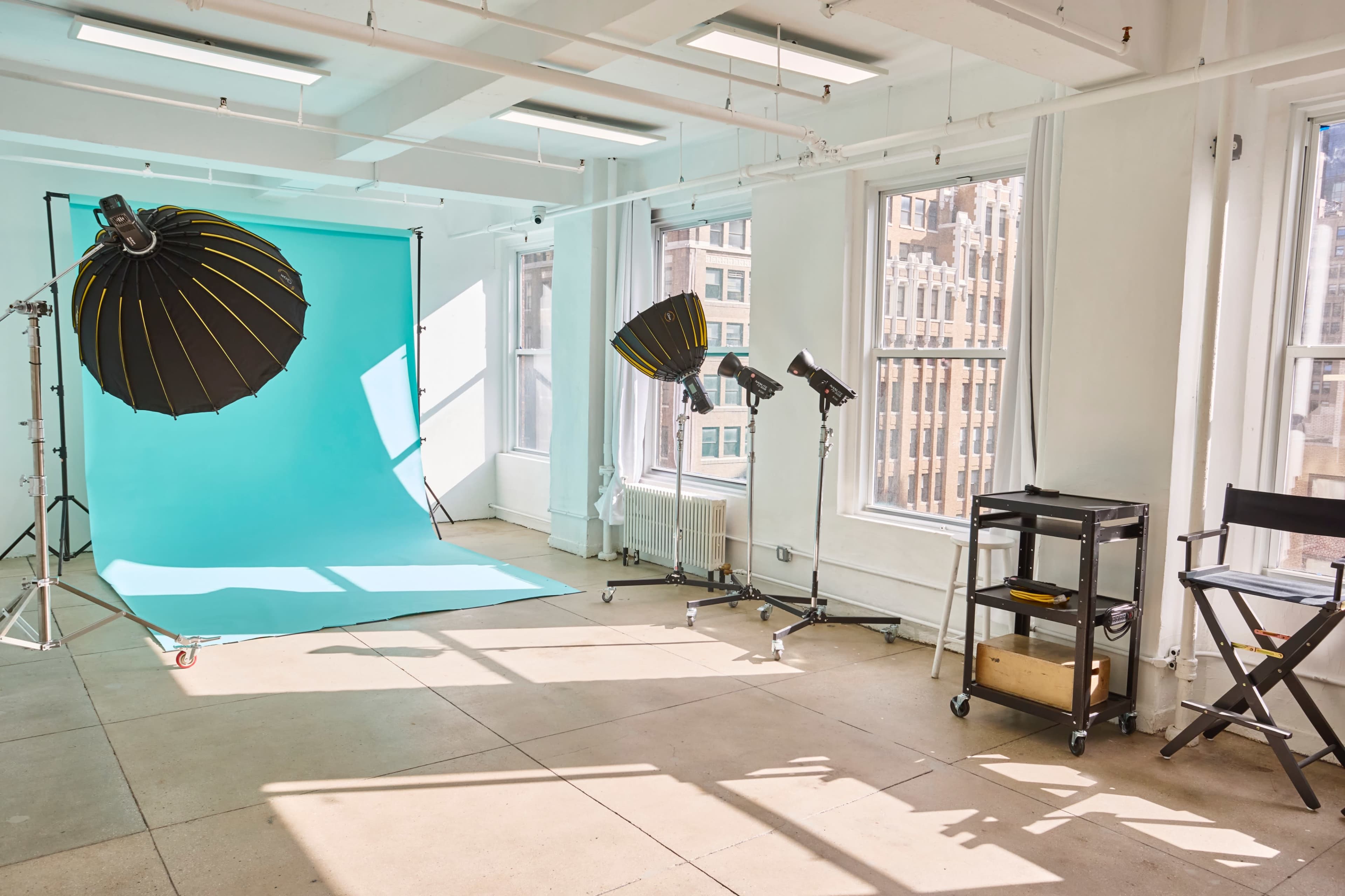The image shows a spacious photography studio outfitted with a bright turquoise backdrop, lighting equipment, and a director's chair.