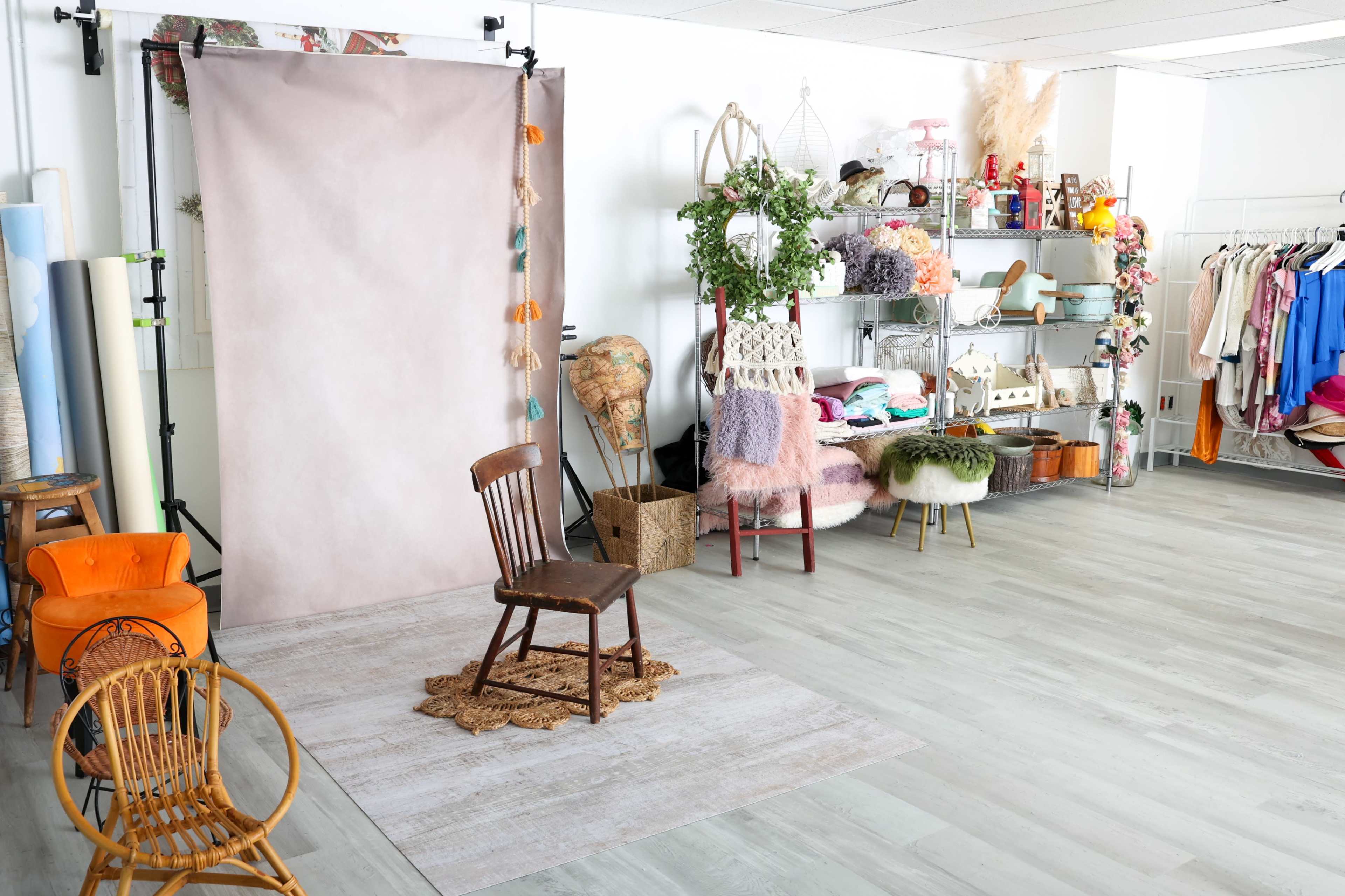 A photography studio with a backdrop, various props, a chair, and neatly arranged shelves filled with colorful items and clothing.