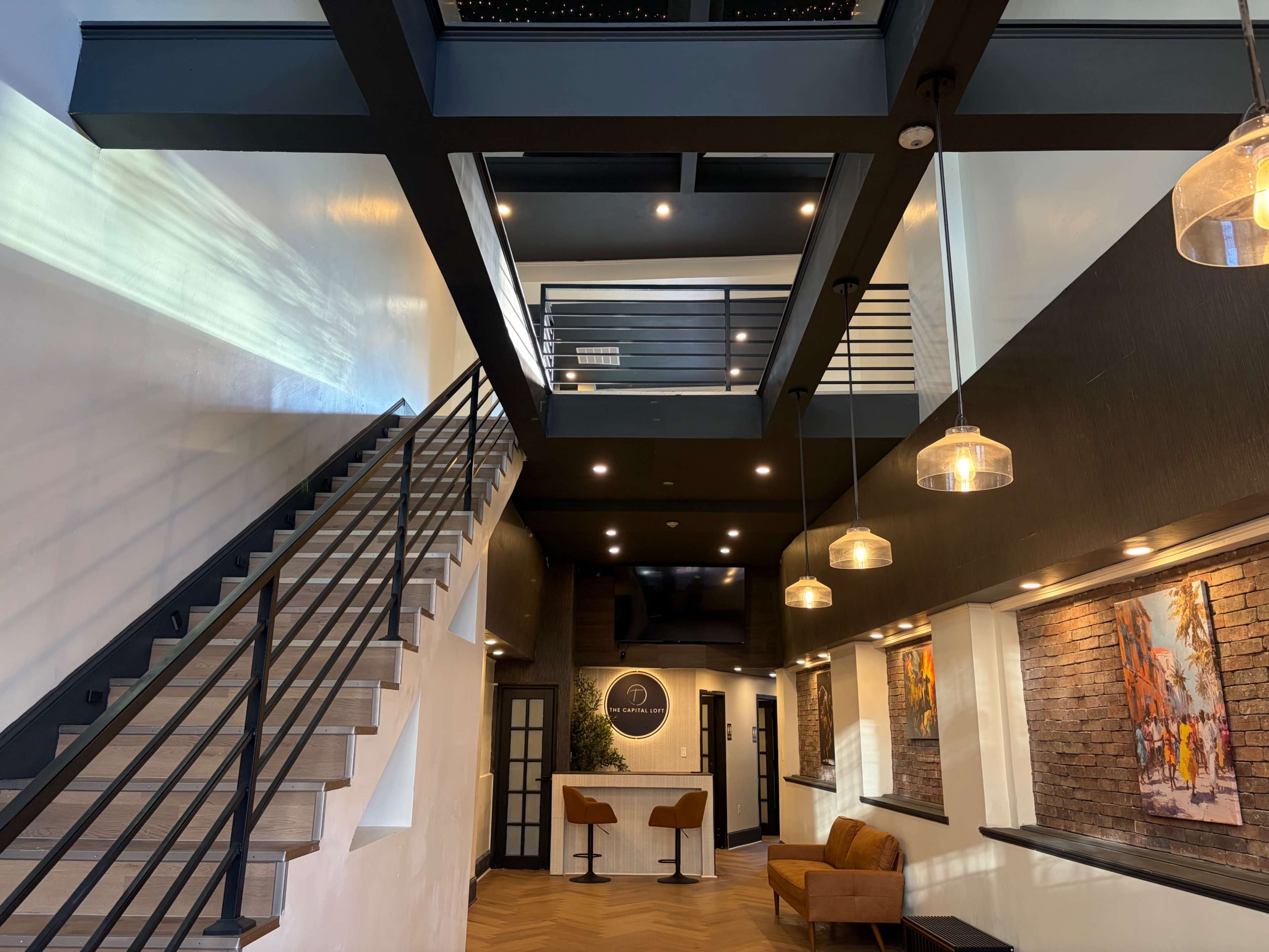 The image shows a modern interior space with a staircase, a seating area, two bar-style counters, and large pendant lights.