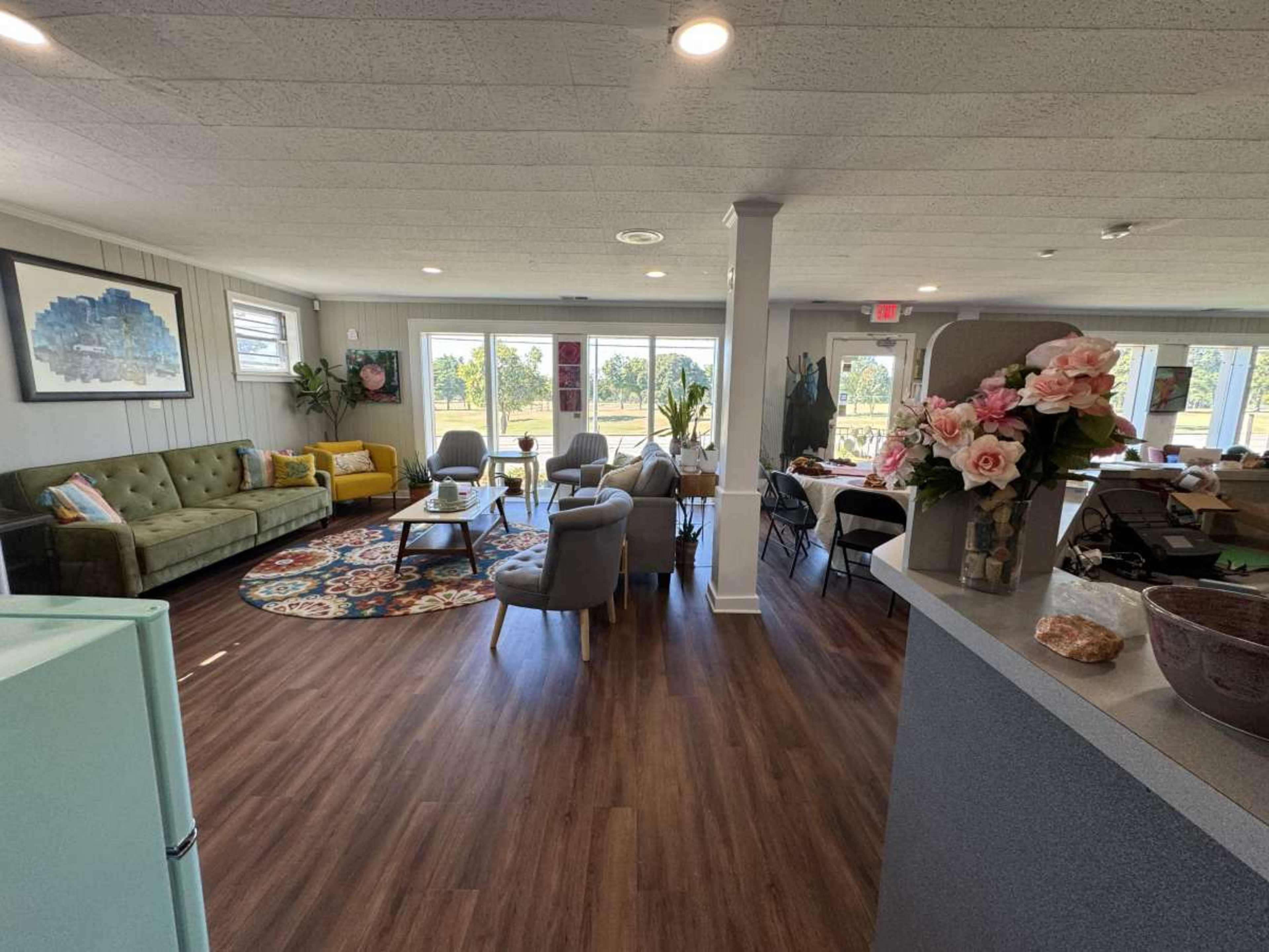 The image shows a bright, open lounge area with a mix of seating options, large windows that let in natural light, and decorative plants.